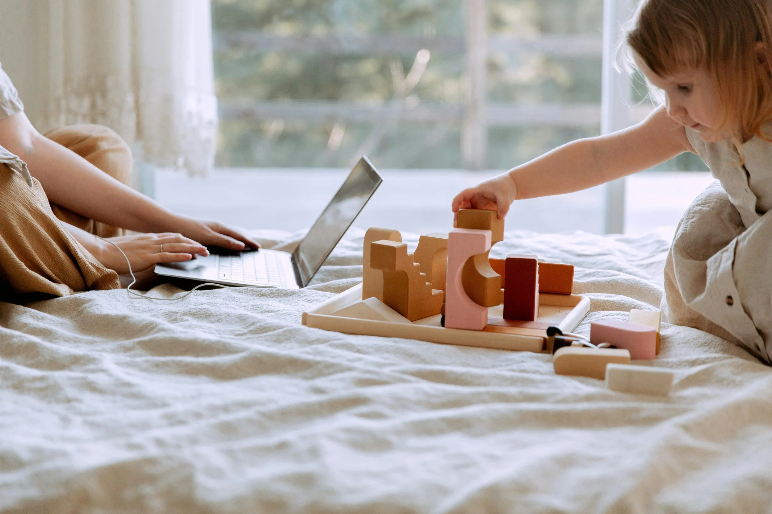 A kid playing with wooden toys on the bed