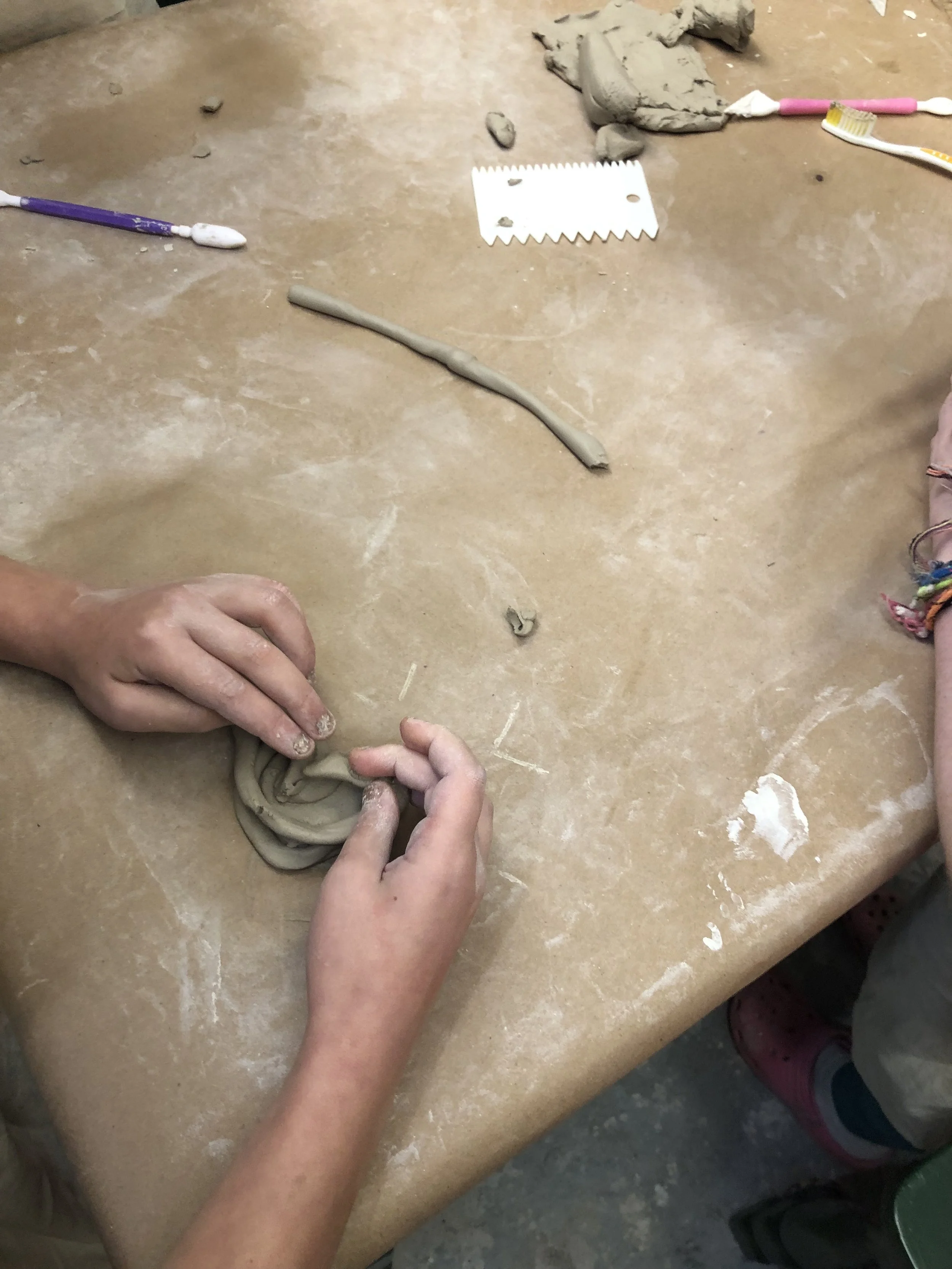 Children making pottery with clay on a work table, with toothbrushes and a clay comb nearby.