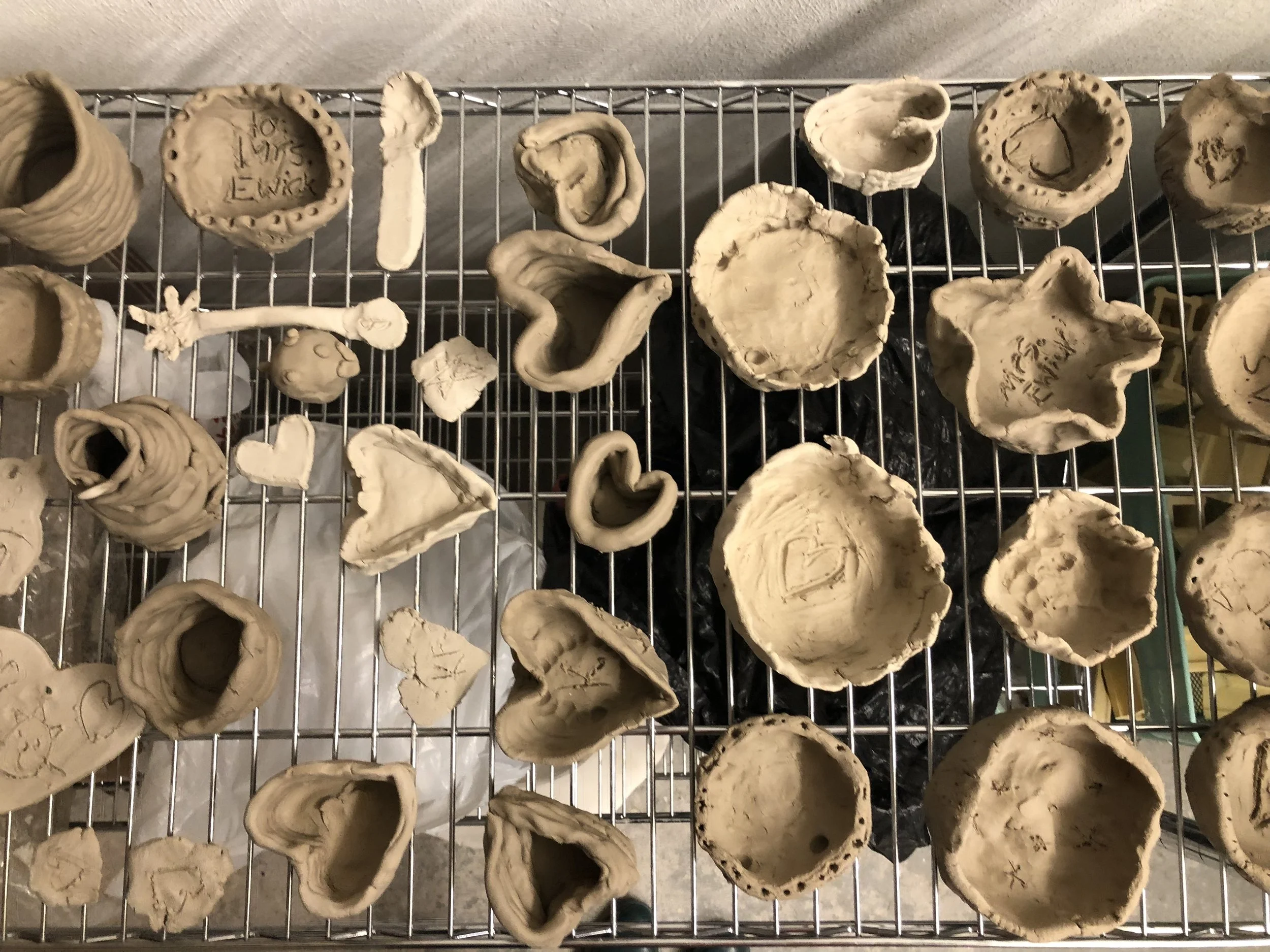 Assorted clay bowls and dishes on a metal wire rack, some with inscriptions or markings inside.