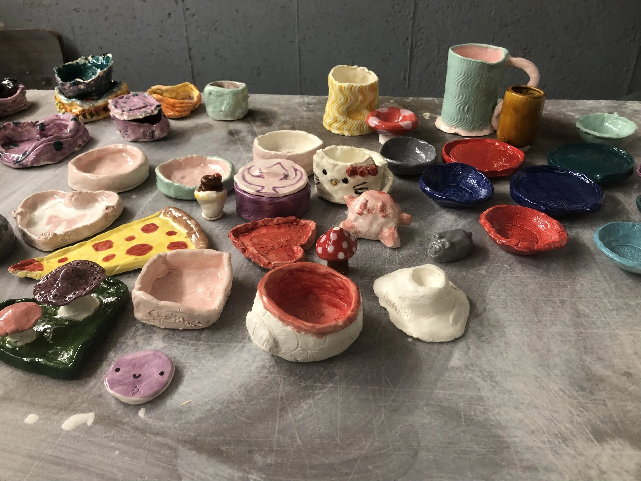 Colorful handmade ceramic pottery including bowls, mugs, small sculptures, and decorative items arranged on a table.