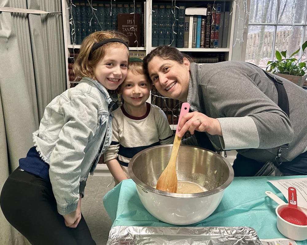 Children and an adult laughing together over a bowl of challah dough.
