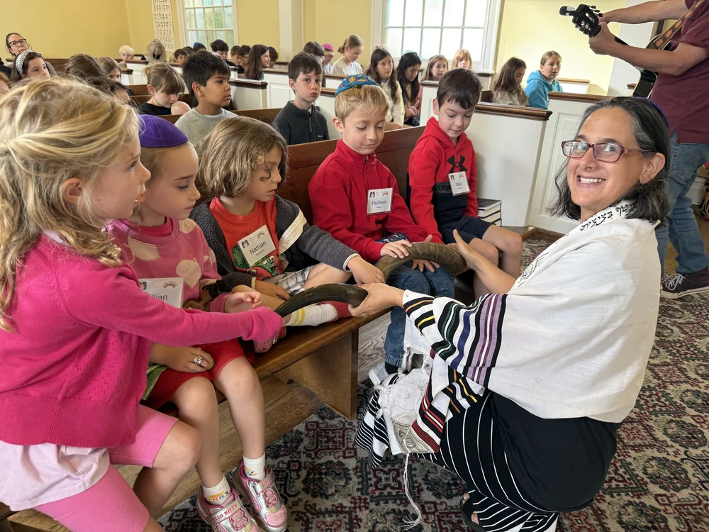 A rabbi surrounded by a group of young children in the Community Room.