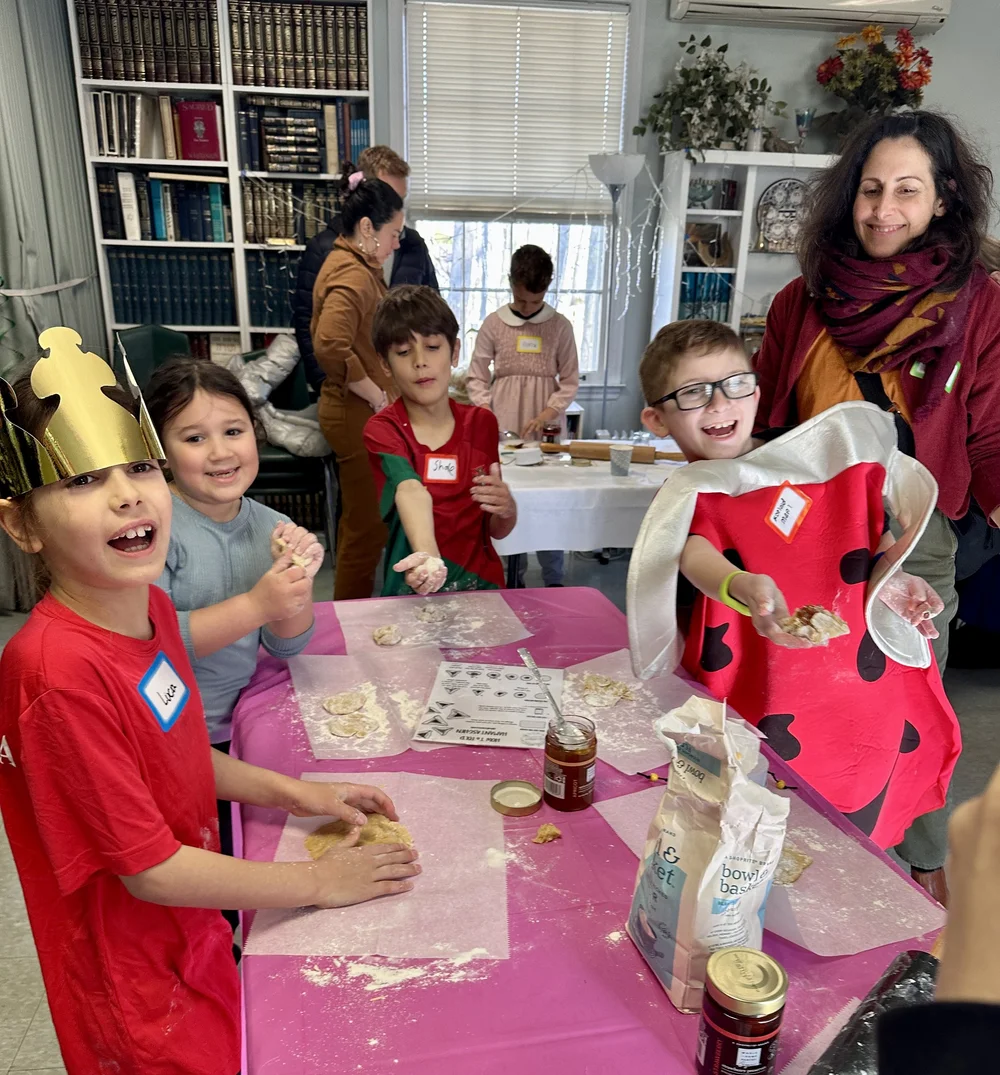 Young children in paper crowns making hamantaschen at a table.