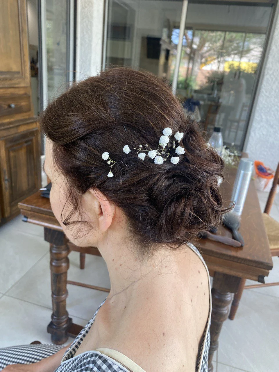 A woman with short curly brown hair styled in an updo, decorated with small white baby's breath flowers.