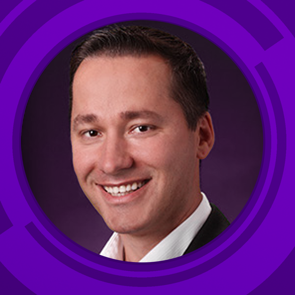 Headshot of a smiling man with dark brown hair, wearing a white shirt and dark jacket against a purple circular background.