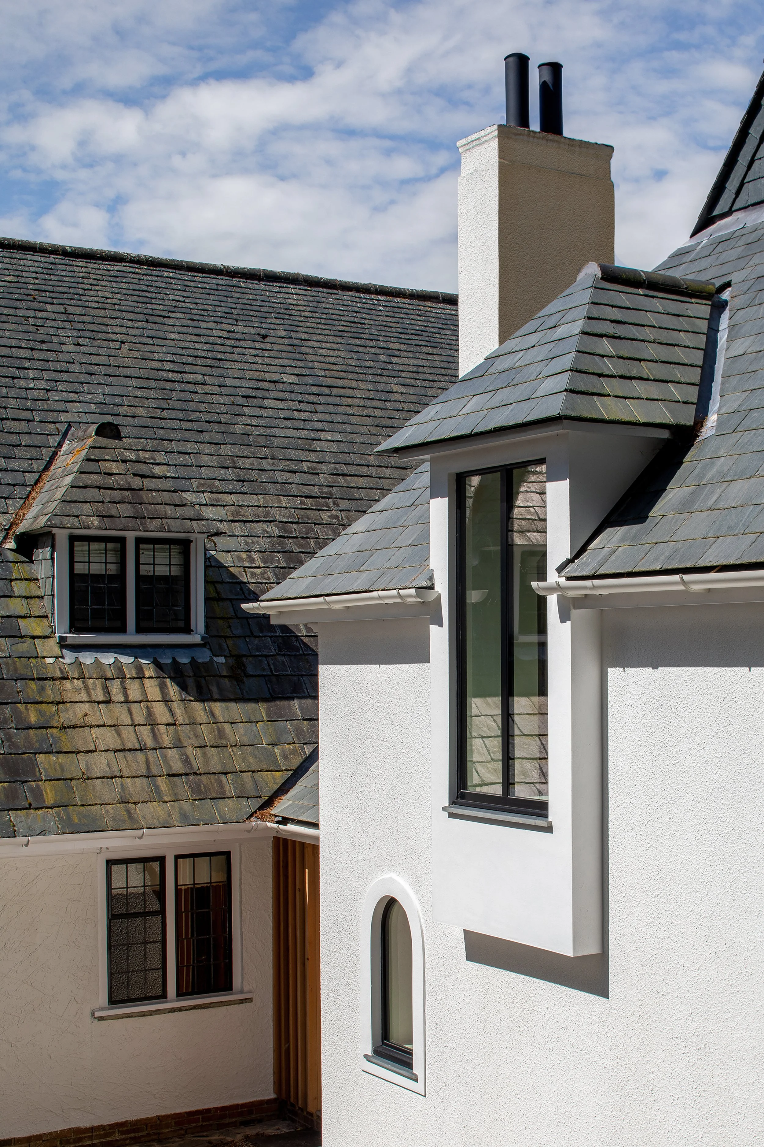 Architectural exterior detail by Coal Cornwall, featuring crisp white roughcast rendered walls, natural slate roof tiles, a white chimney stack, and modern black-framed dormer windows.