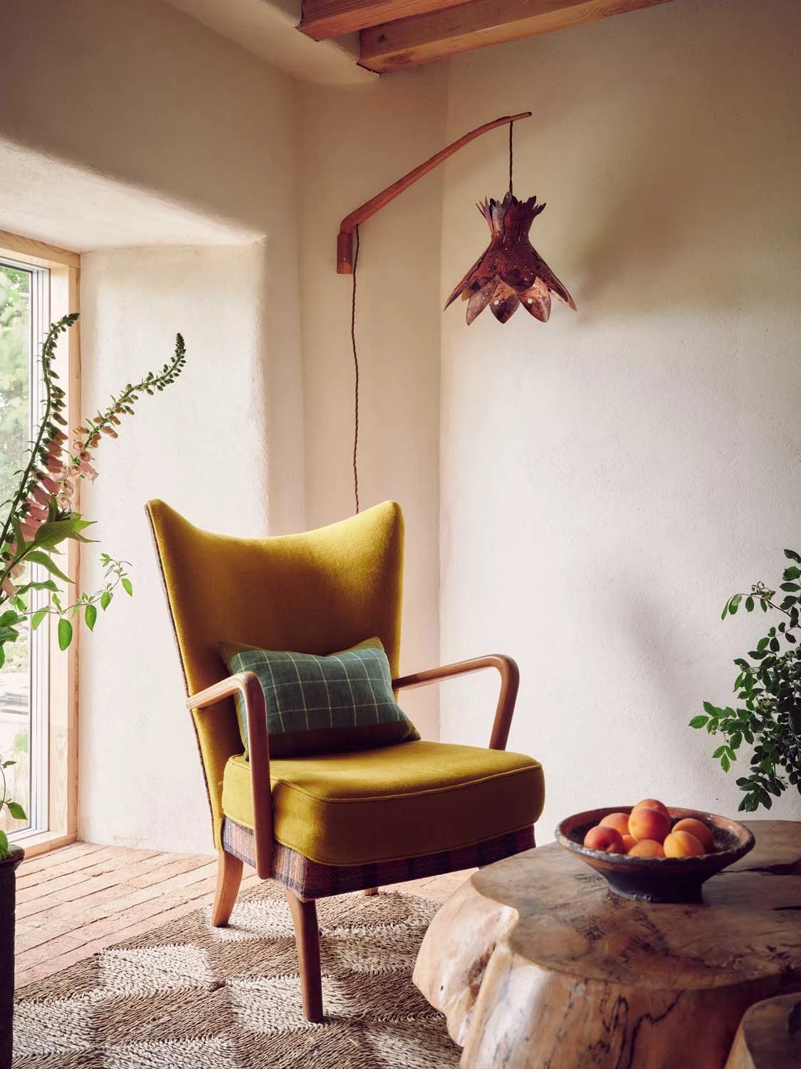 Cozy reading corner by Coal Cornwall, featuring a mid-century yellow wingback armchair, a curved wooden wall-mounted copper light fixture, a live-edge wooden coffee table, and natural plaster walls.