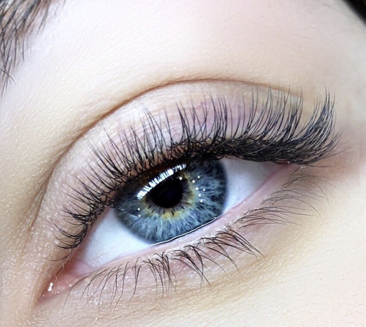 Close-up of a human eye with blue and green iris, long eyelashes, and light skin around the eye.