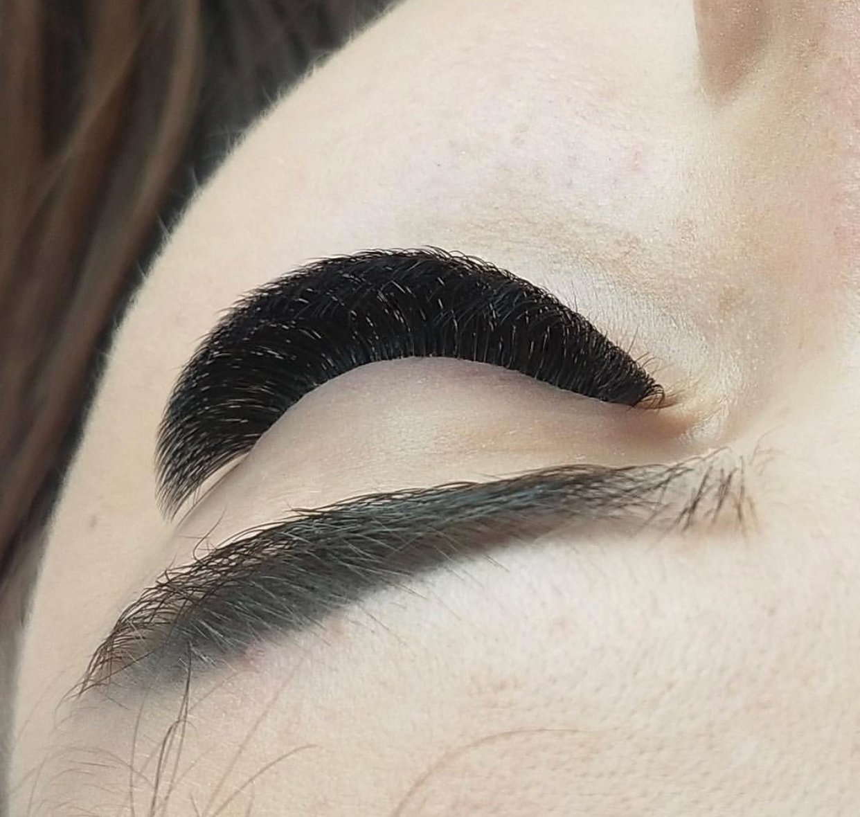 Close-up of a closed eye showing long, lifted, and curled eyelash extensions and well-defined eyebrow with makeup