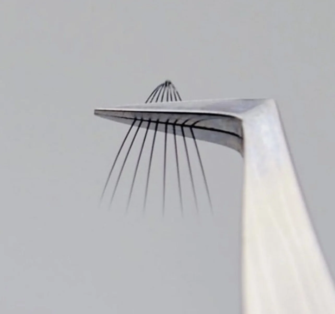 Close-up of a scale model of a suspension bridge, focusing on the top of one tower with suspension cables extending downward.