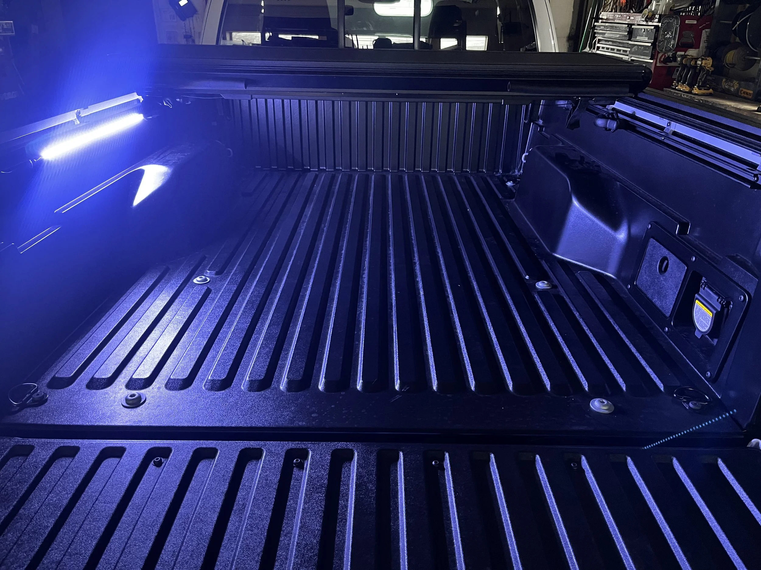 Empty truck bed illuminated with blue LED lights, showing a textured surface and side compartments. Bed liner and bright blue custom blue LED Lights.