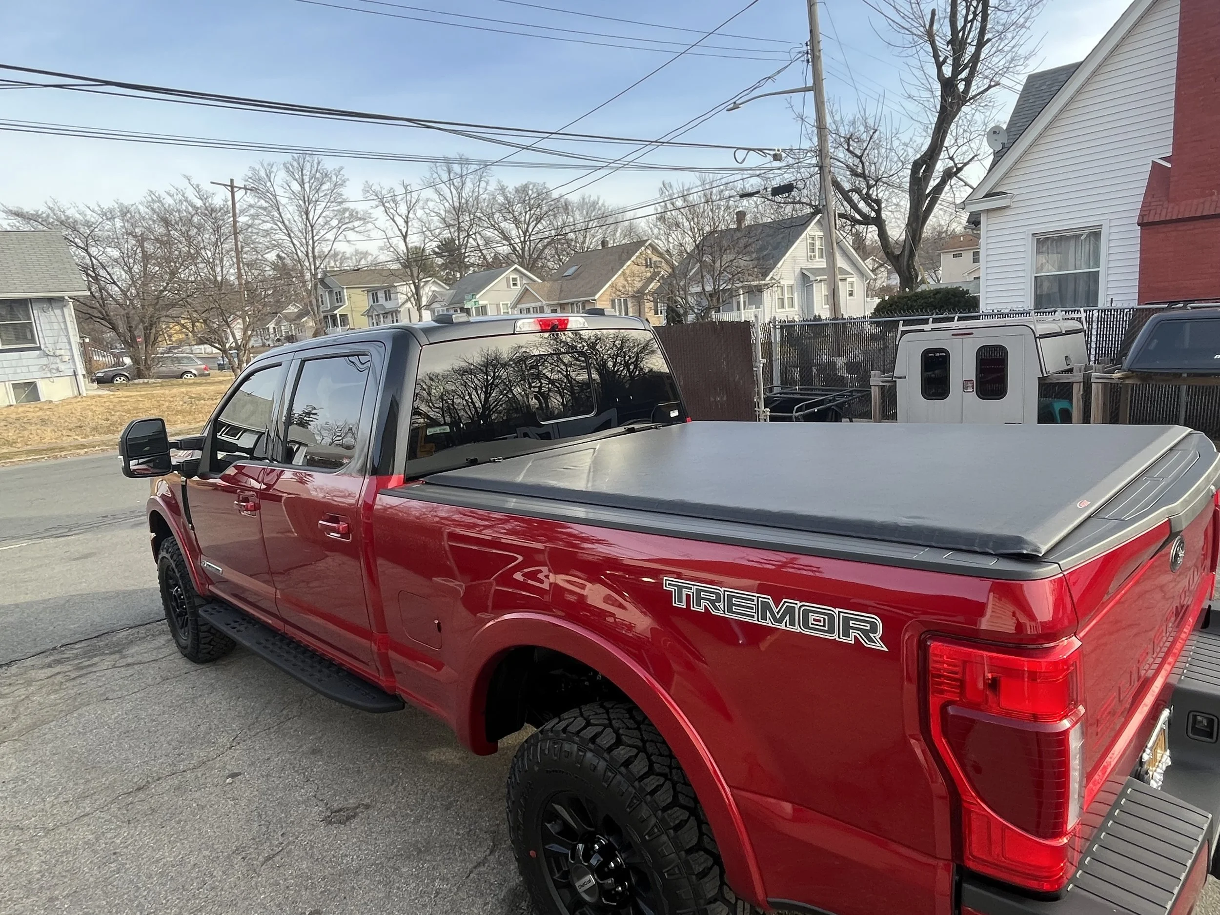 Red Toyota Tundra pickup truck with TREMOR badge parked on a residential street during daytime, with houses and trees in the background. Access Lorado vinyl tonneau cover on Ford F-250.