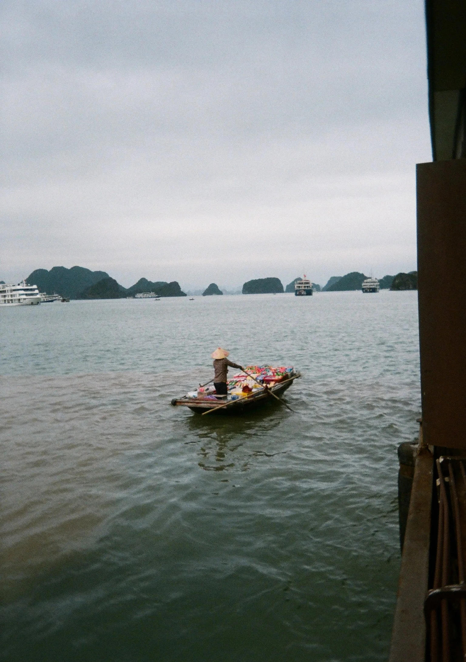 A person rowing a small boat on a body of water with boats and islands in the background.