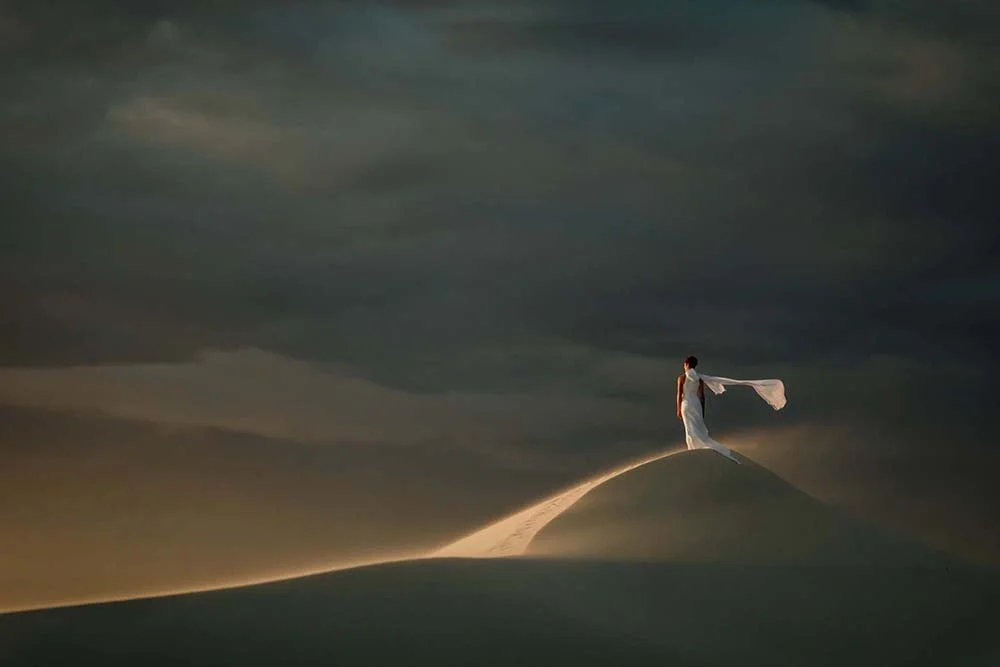 Sunset photo of a bride standing in the wind on a dune
