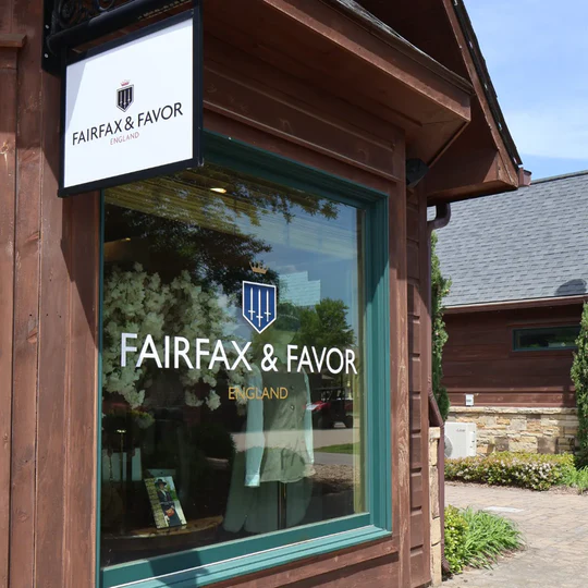 The exterior of a wooden building with a large window displaying a sign for Fairfax & Favor, England. There is a smaller sign above the window also displaying the Fairfax & Favor logo and text.