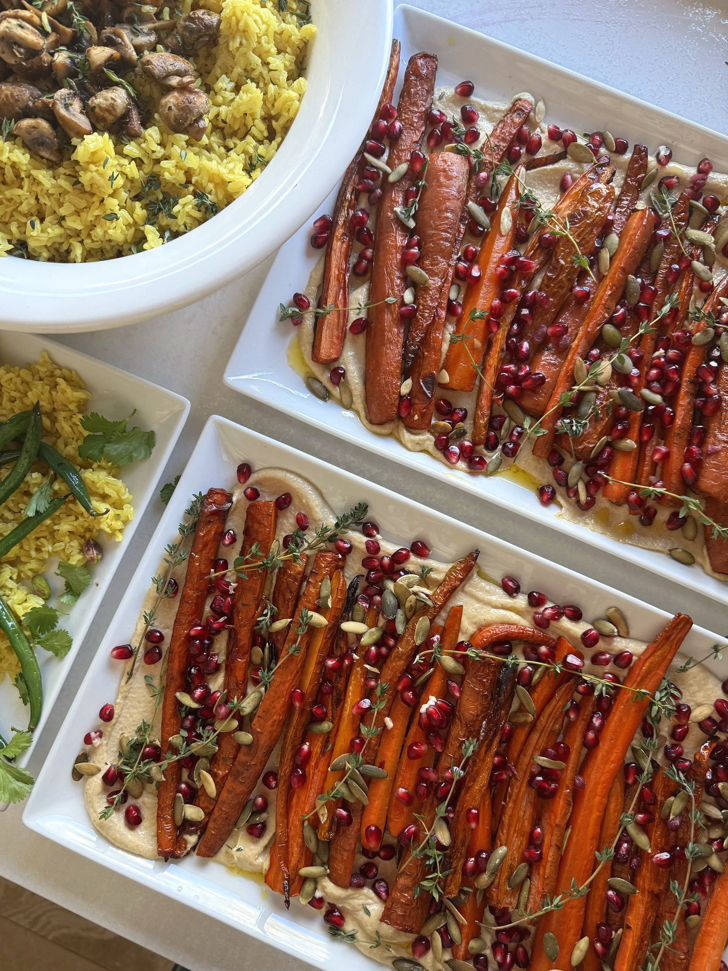 Roasted carrot and pomegranate appetizer with herbs and seeds, served on rectangular white plates.