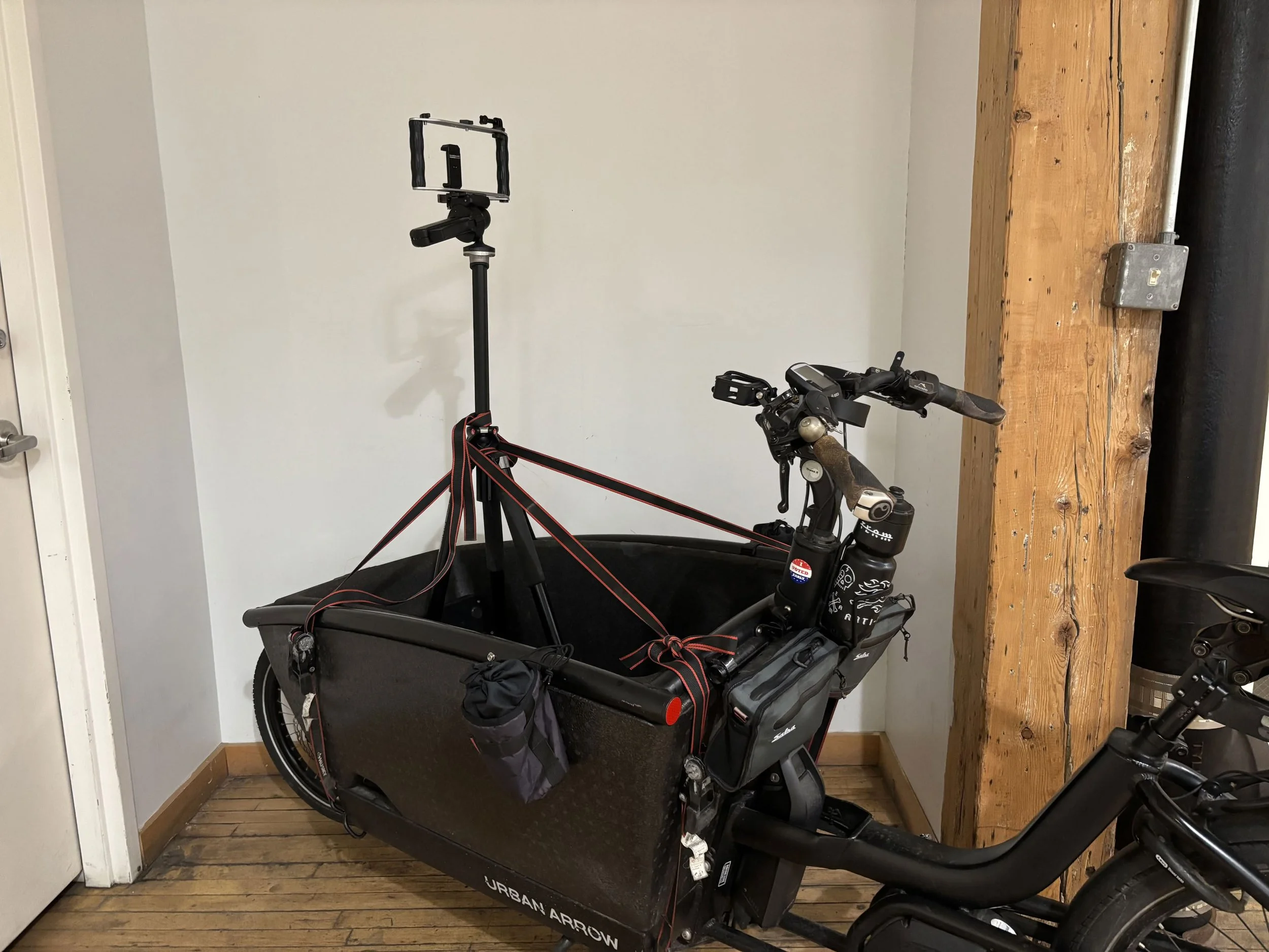 A tripod with an iPhone camera mount wretch strapped into the front bucket of a cargo bike for a rolling steady cam shot.