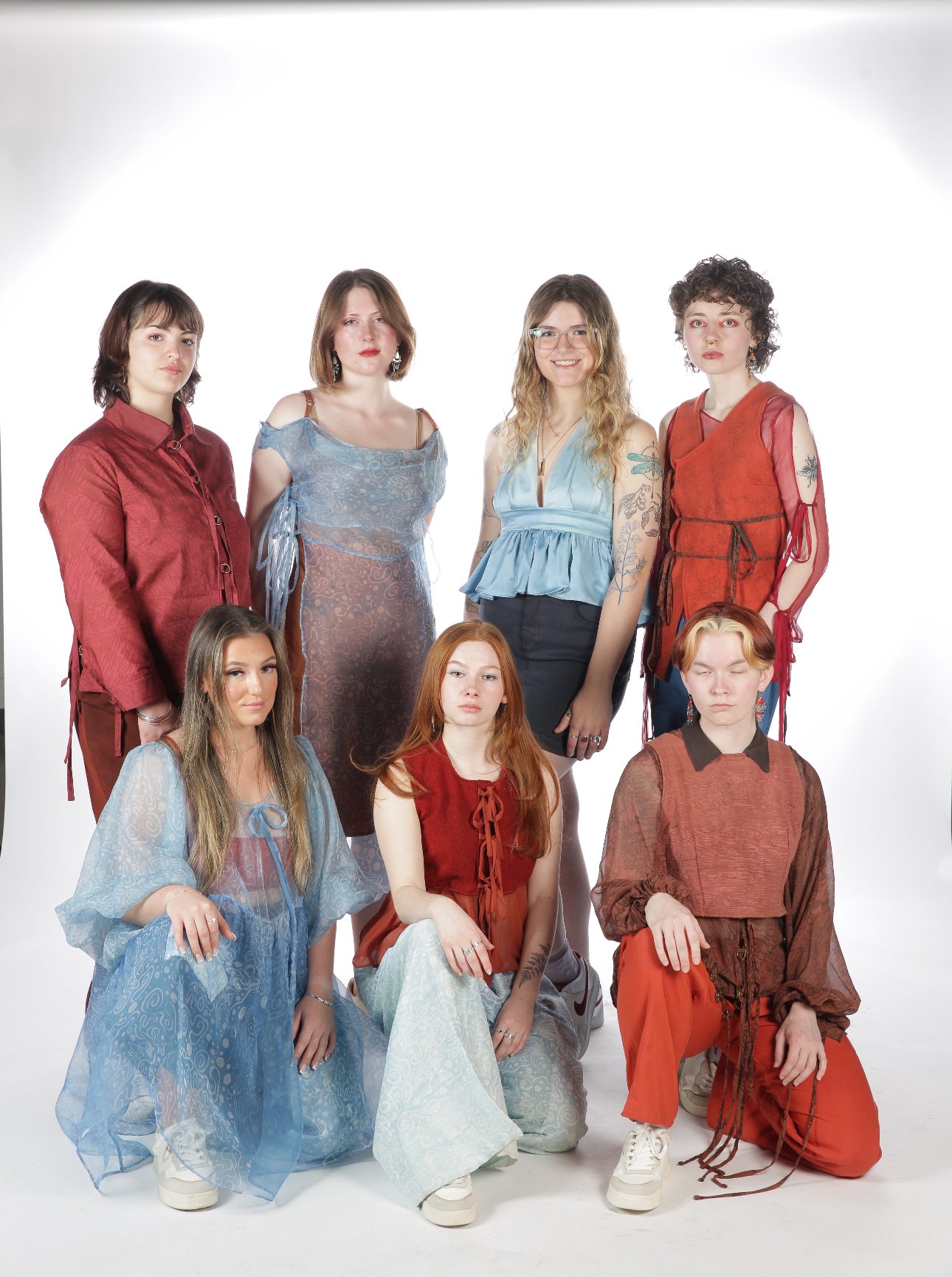 Group of eight women posing together in fashion-forward outfits on a white background.