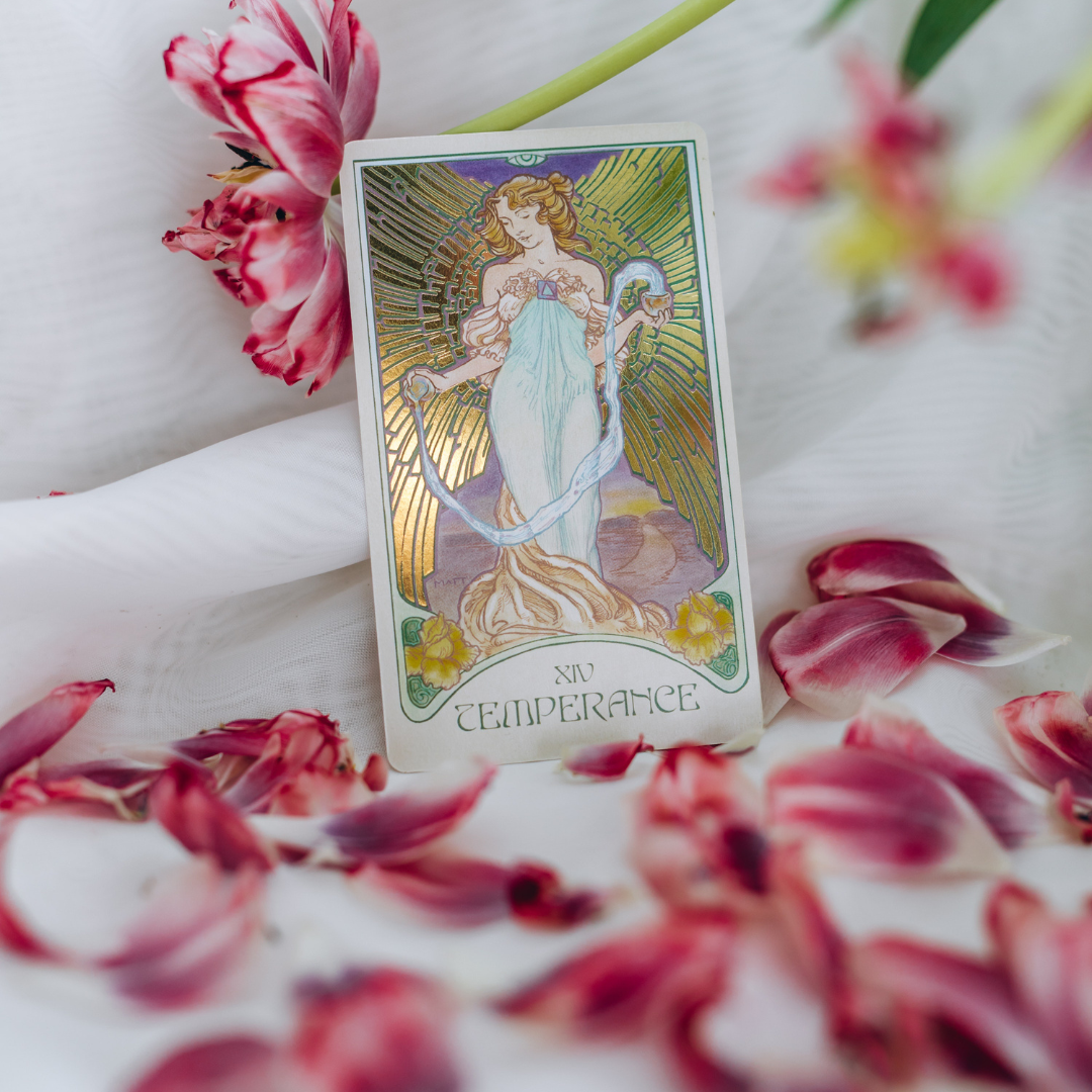A tarot card titled "Temperance" with an illustration of a woman holding two cups, standing amidst a radiant background, surrounded by pink and white flower petals.