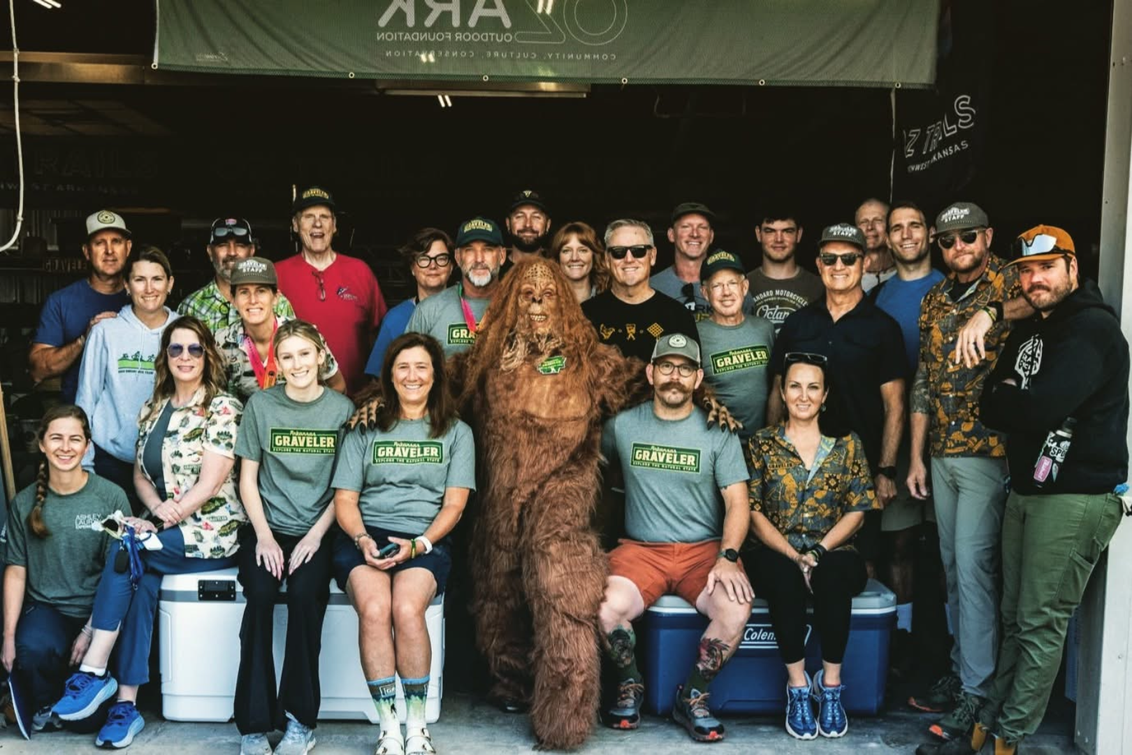 Group of people gathered outdoors, some wearing matching 'Gravelers' t-shirts, posing with a person dressed as a Bigfoot or Sasquatch in the center.