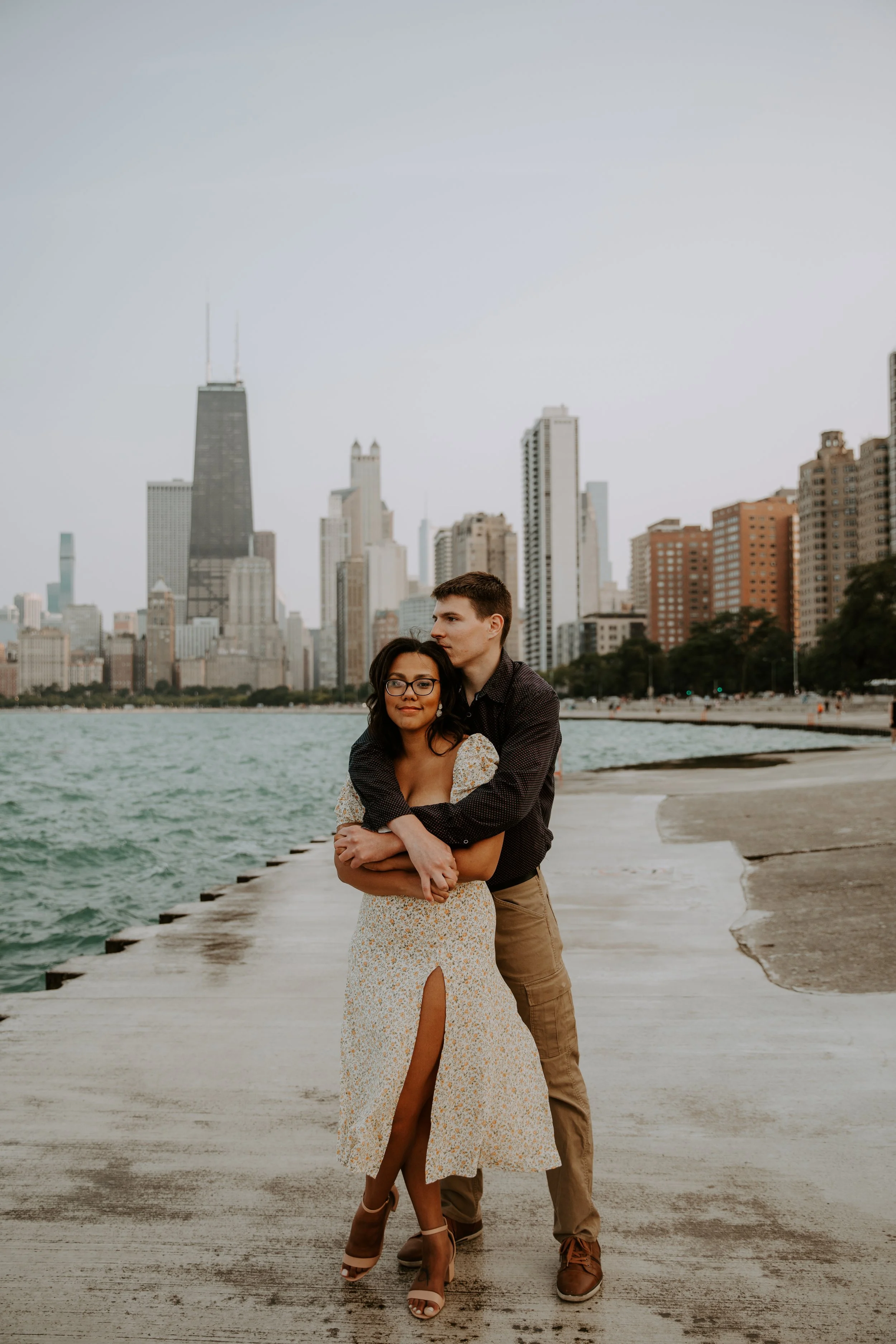 Couple standing beside Lake Michigan with the skyline in the background, embracing.