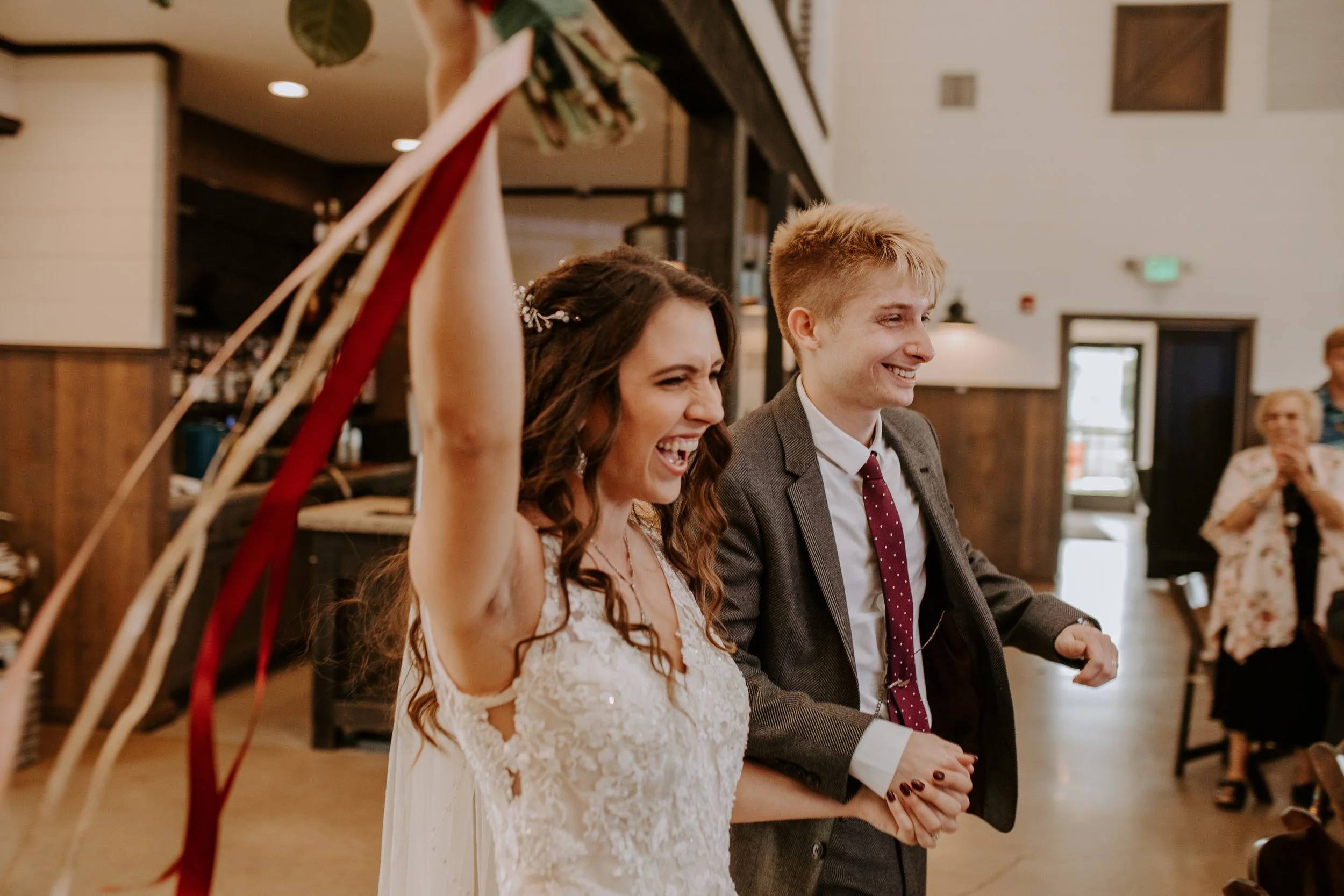 Bride and groom entering their wedding reception, hand in hand, smiling and celebrating with their guests.