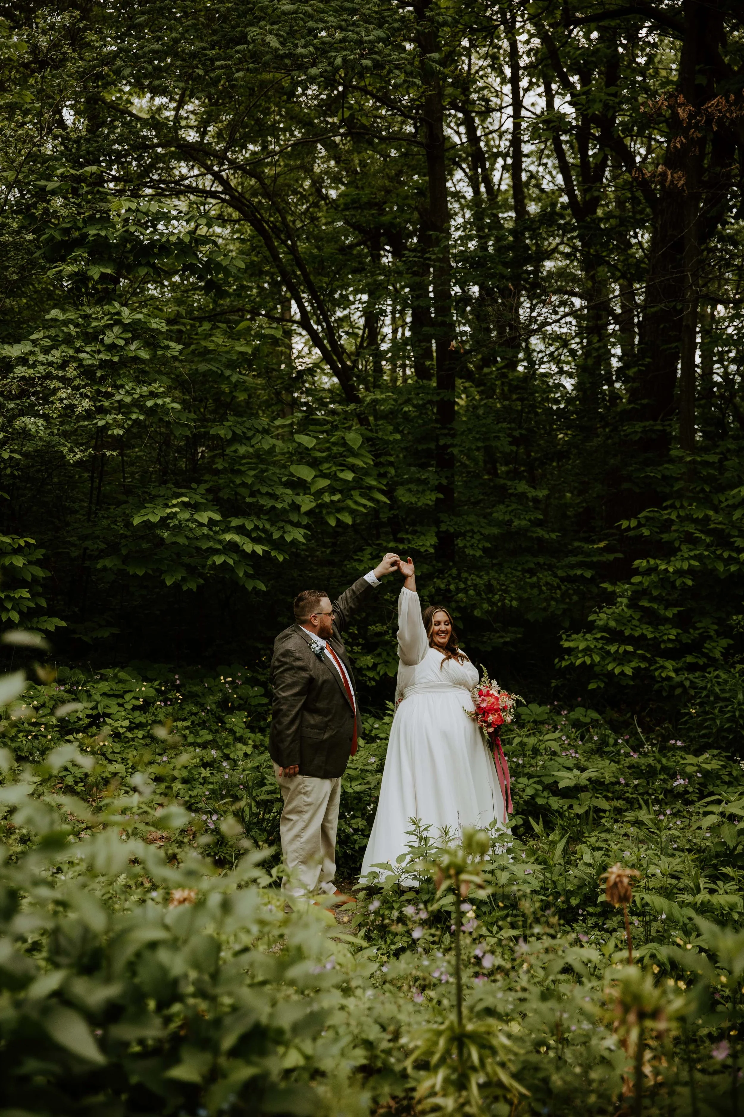 The groom twirls the bride surrounded by greenery.