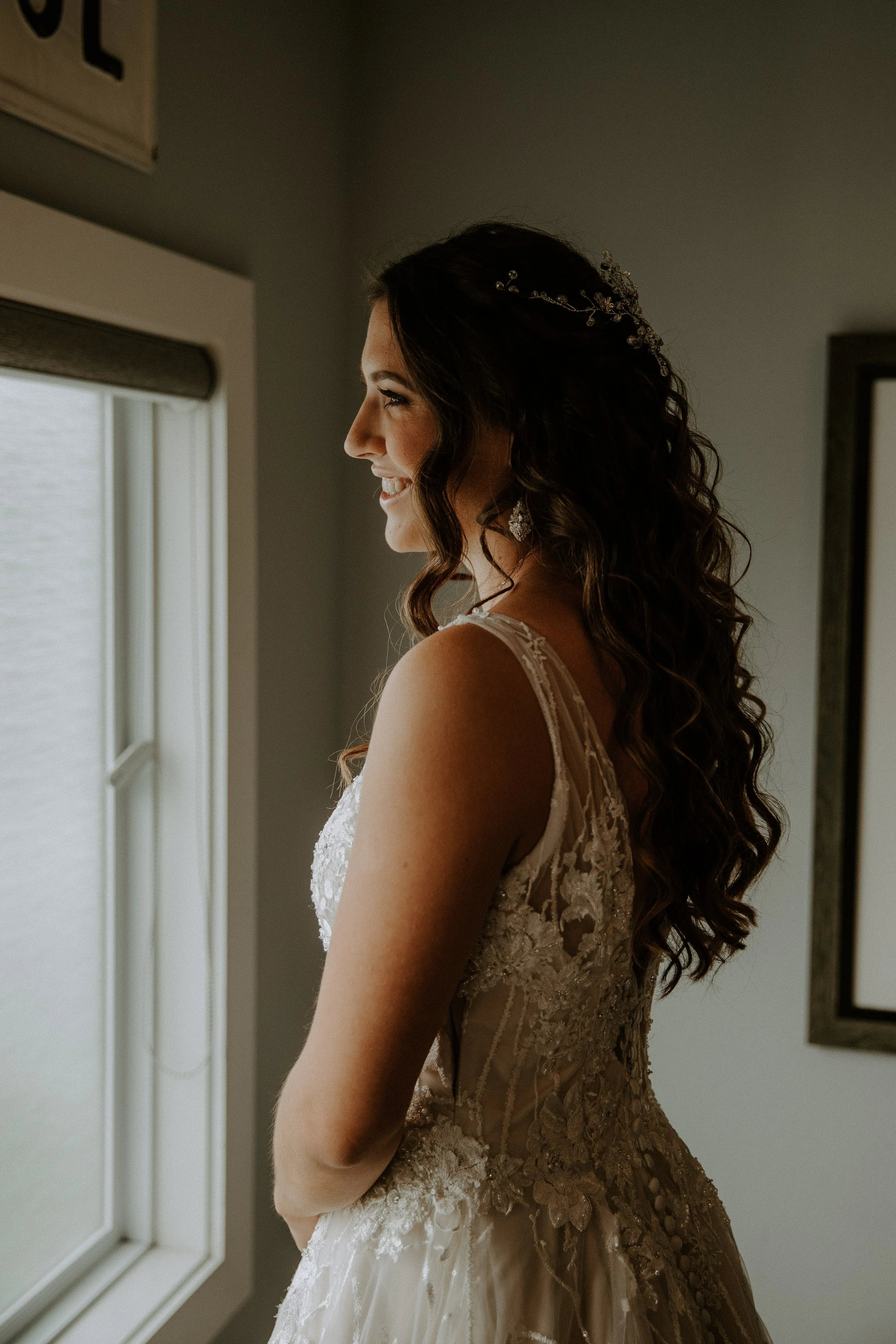 Close-up of the bride's wedding dress and jewelry as she gently holds her veil, highlighting the intricate lace details.
