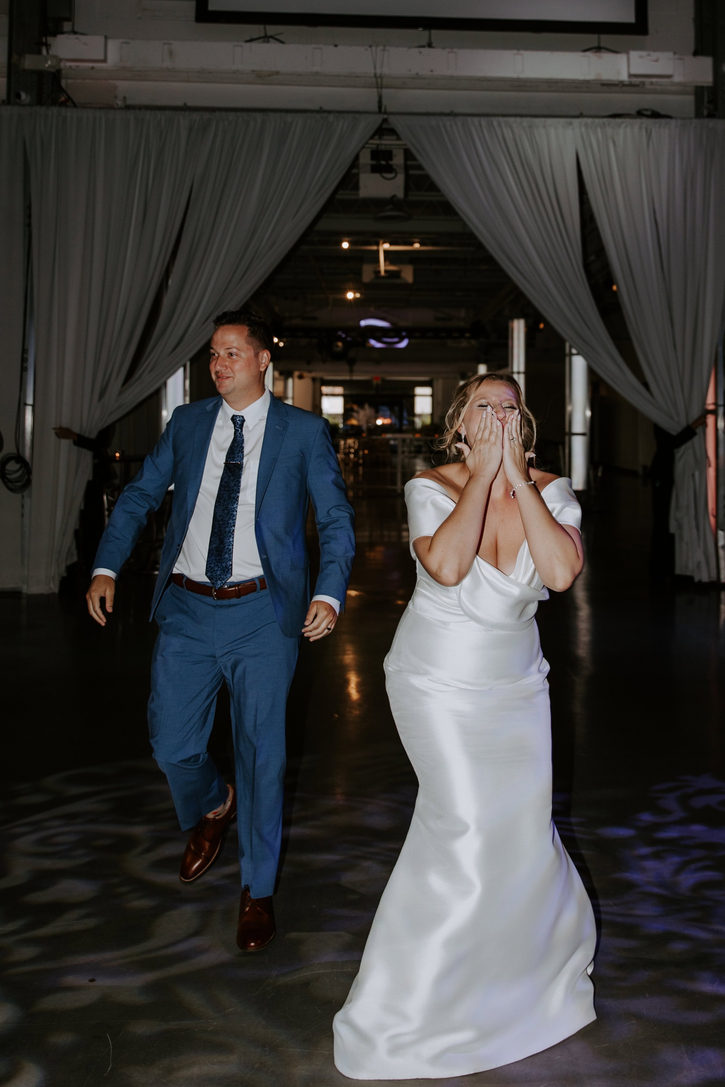 The bride blows a kiss as she walks into the reception with her husband behind her.