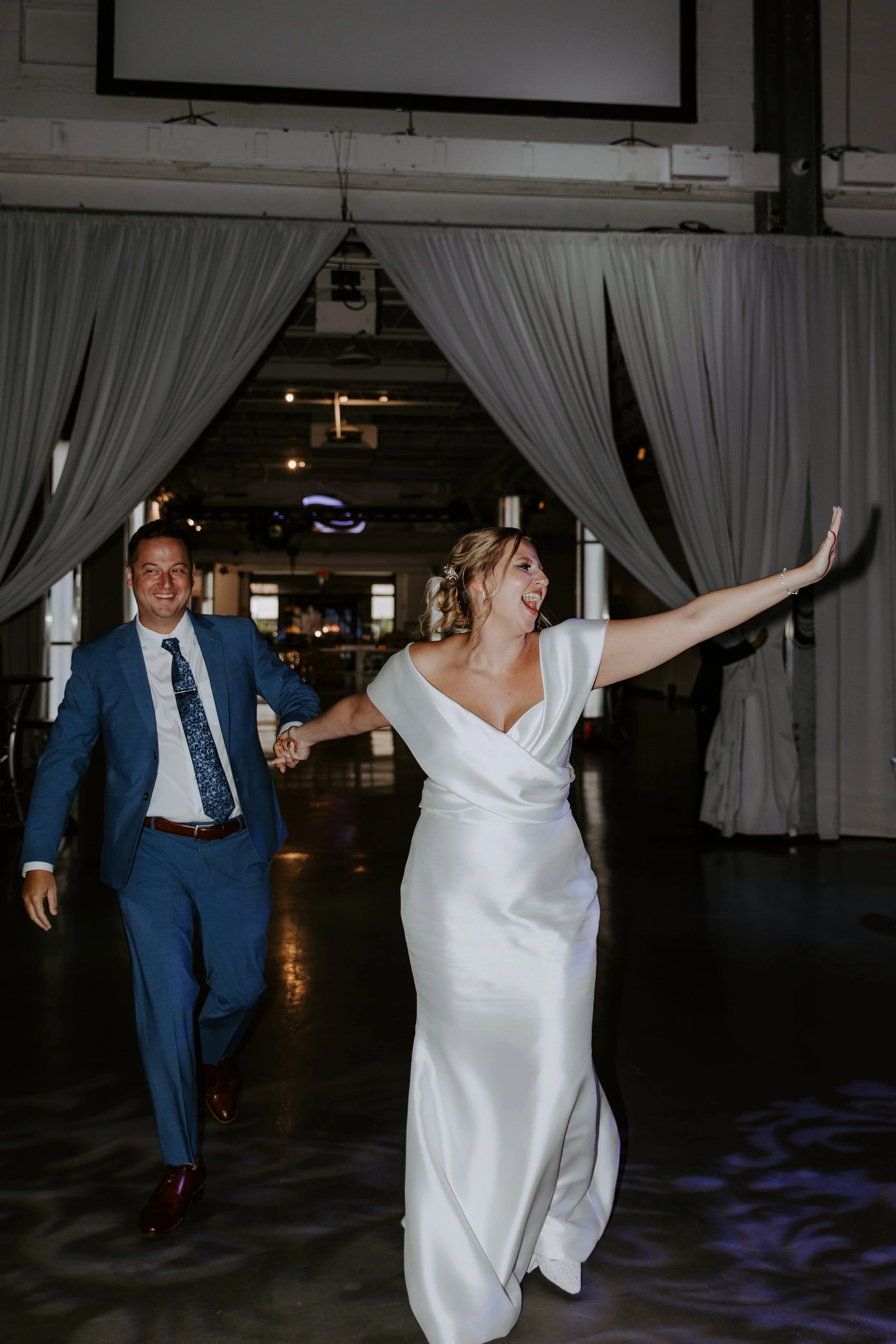 The bride waves as she walks into the reception holding her husbands hand.