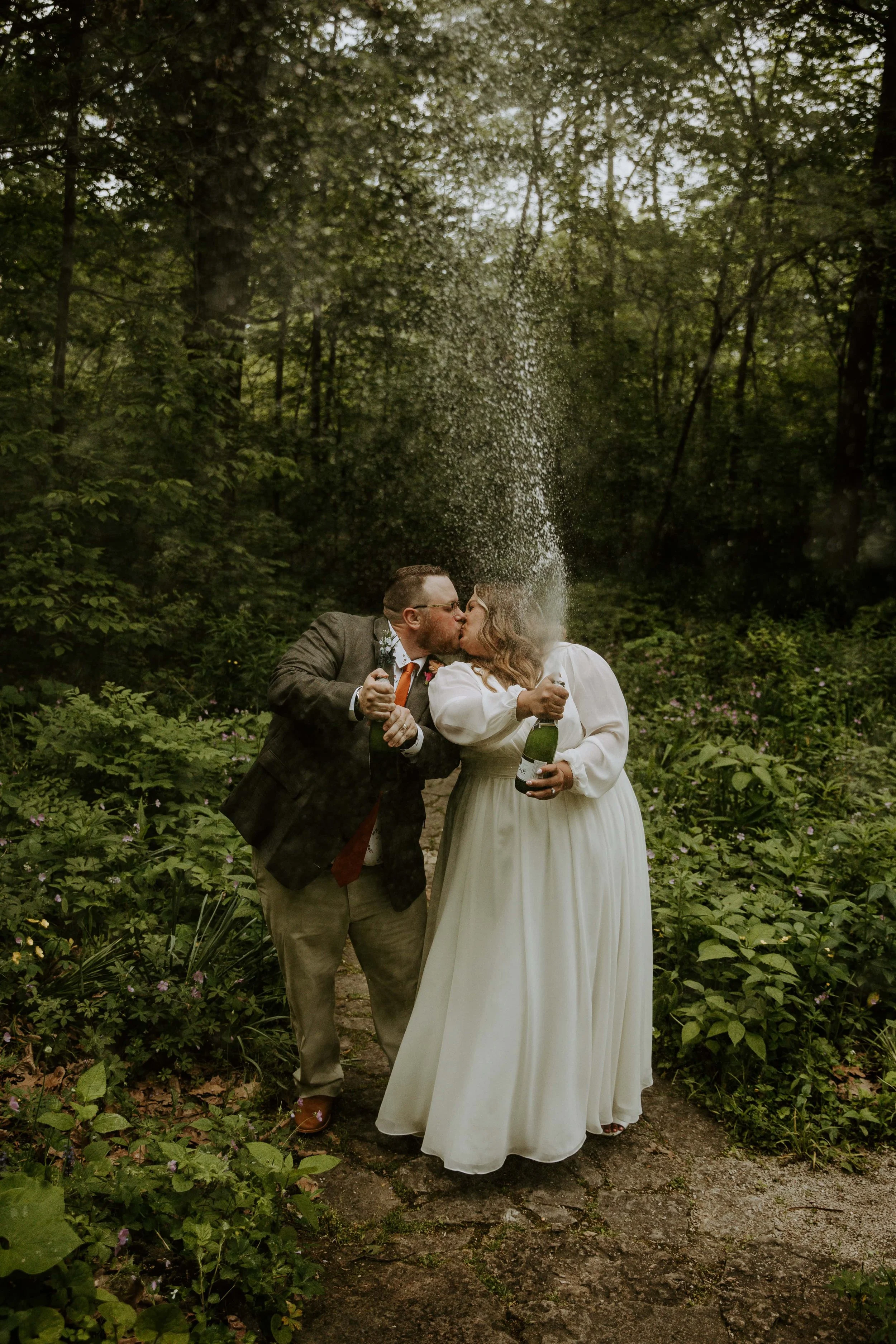 The bride and groom kiss as they each pop a bottle of champagne.