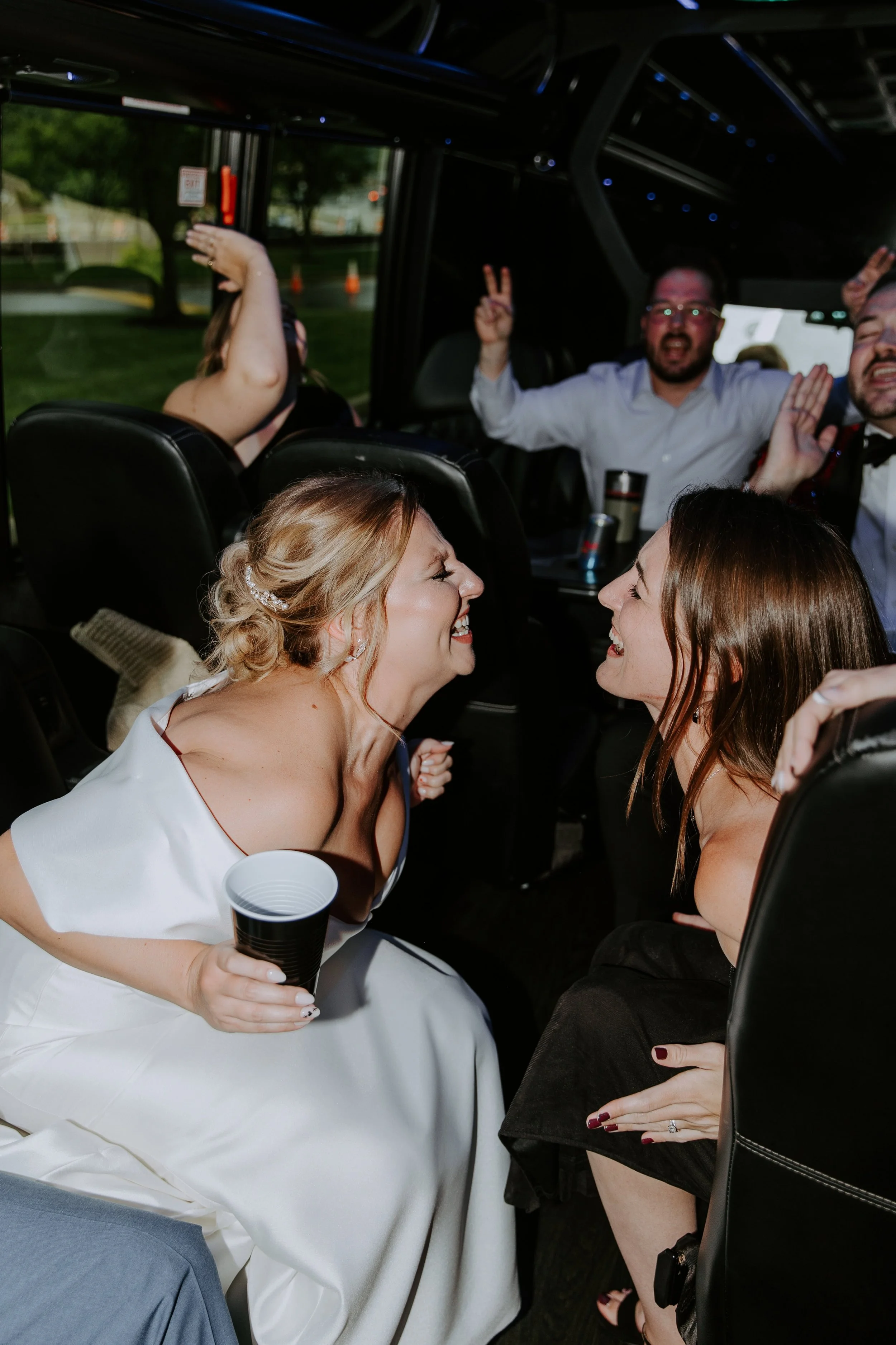 Bride sings with one of her friends on a party bus heading to their wedding reception.