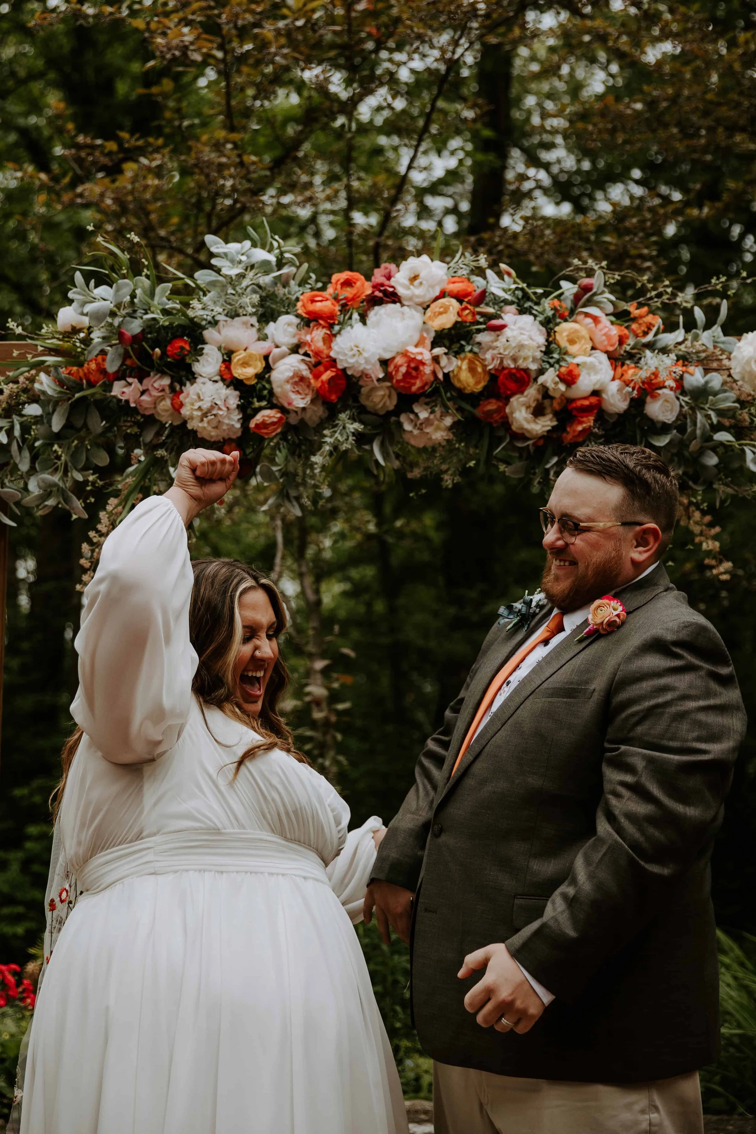The bride throws a fist in the air while the groom laughs after they are officially married.