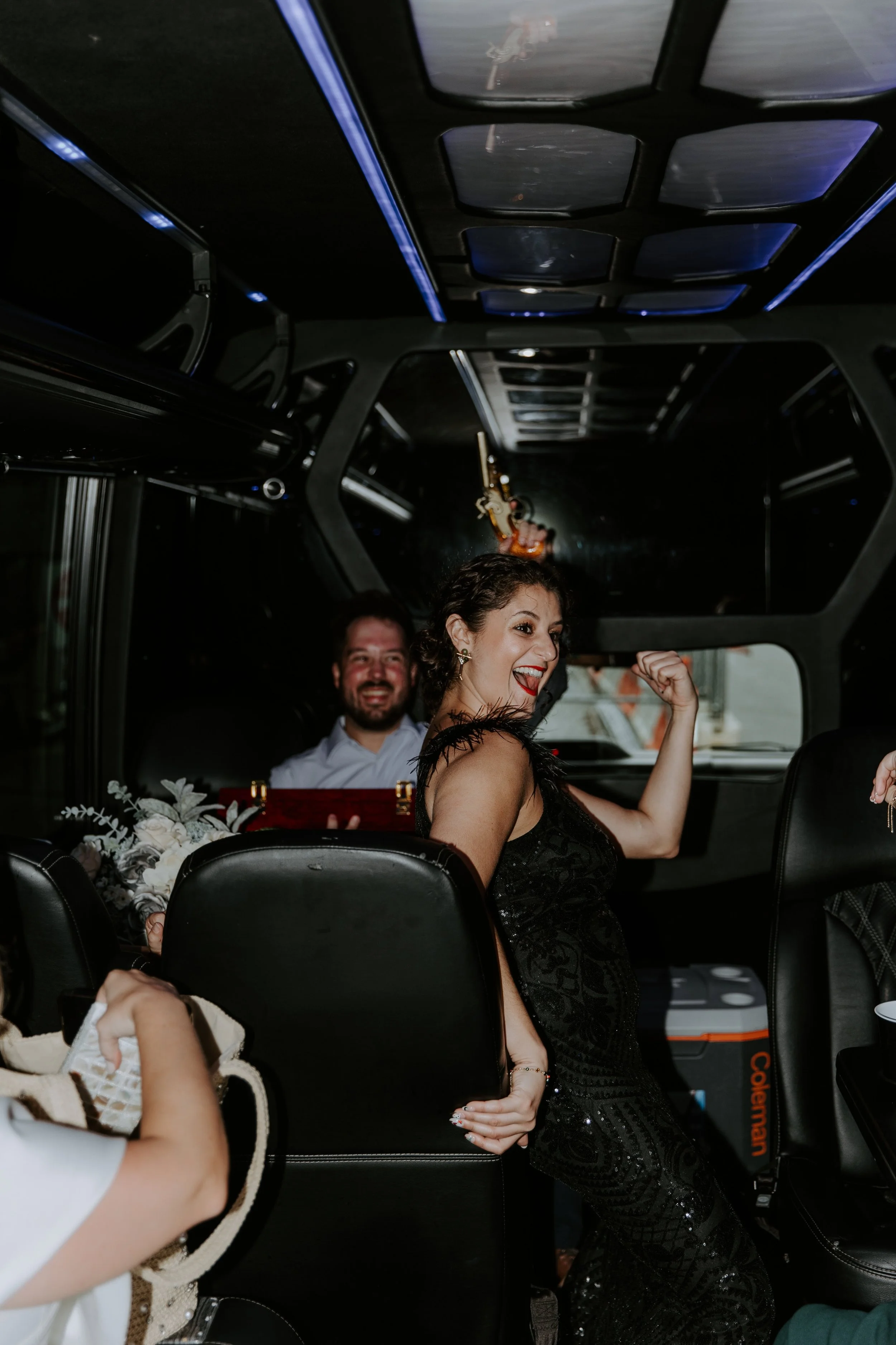 A girl in a black tank top dress with feather sleeves dances on a party bus.
