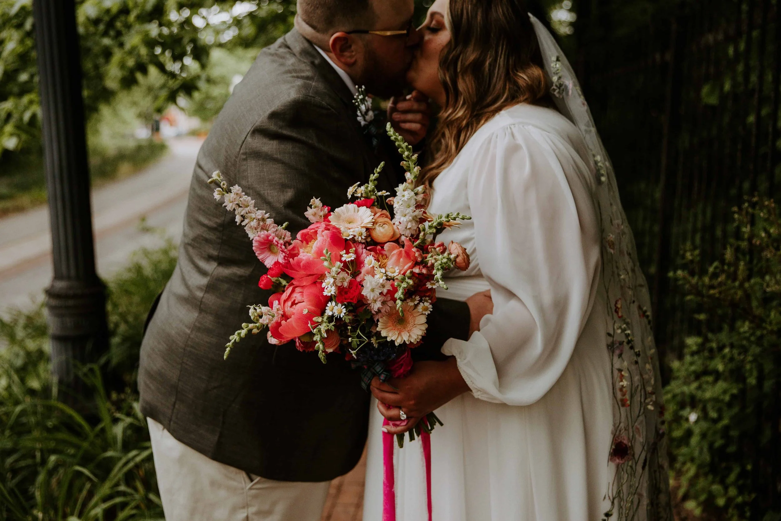 A detail photo of the bride holding her bright pink bouquet as the couple kiss.