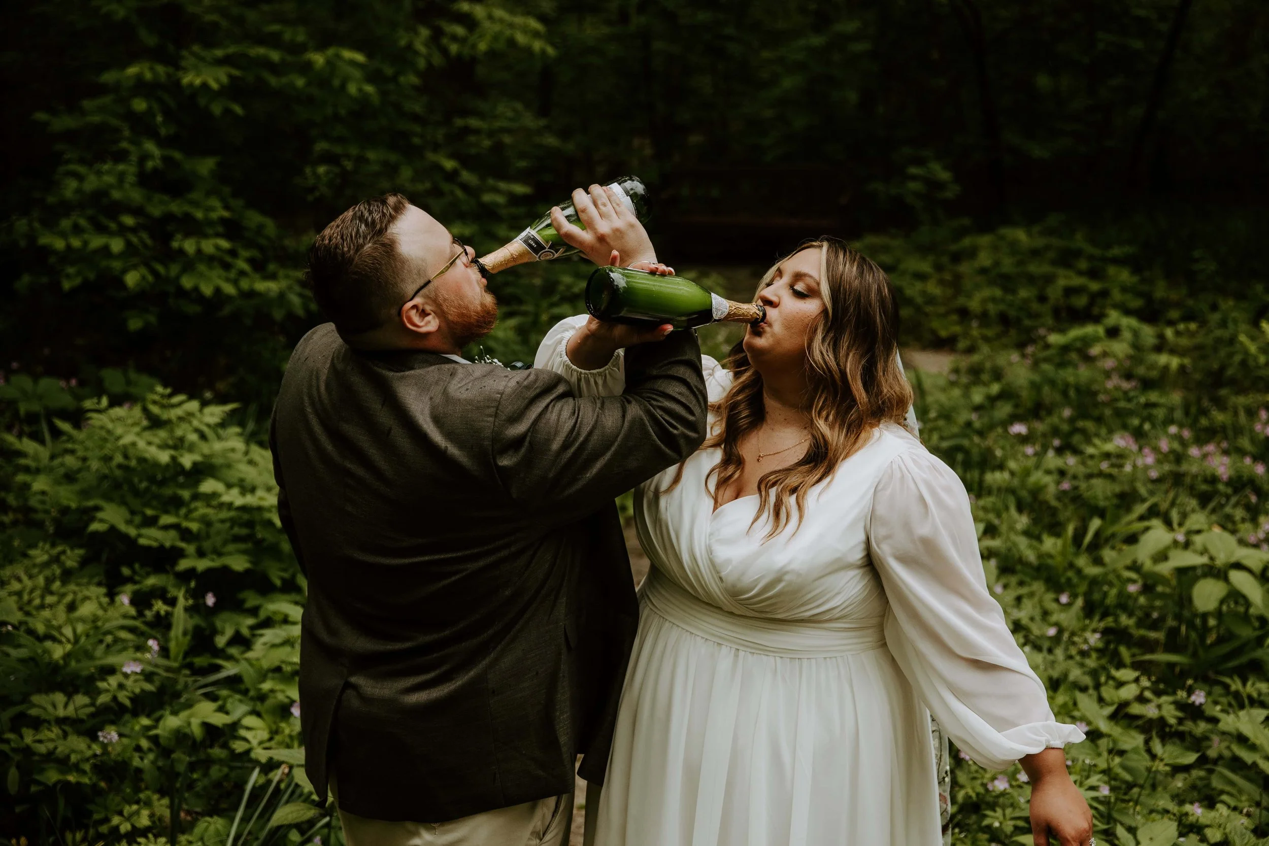 The bride and groom intertwine arms to drink champagne out of the bottle.