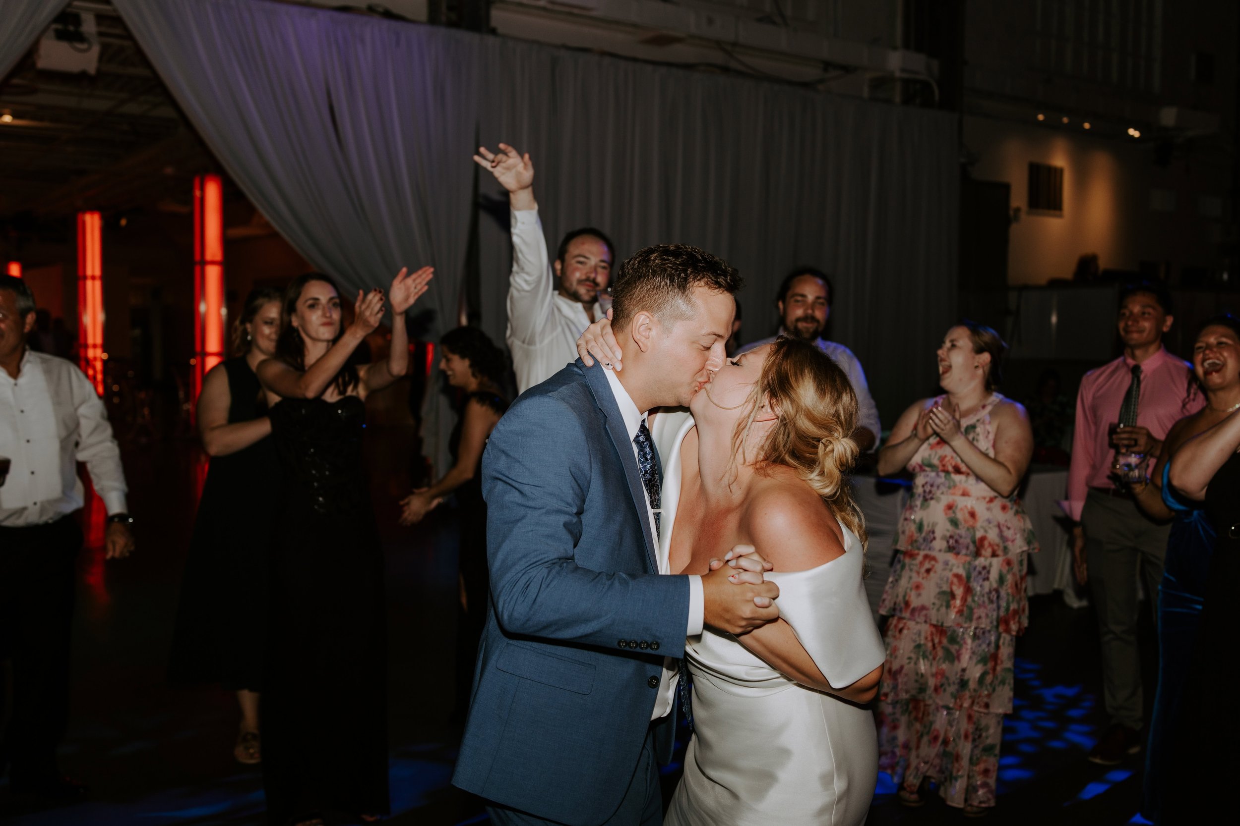 The bride and groom kiss on the dancefloor surrounded by guests at their wedding reception at Crane Bay Event Center in Indianapols.