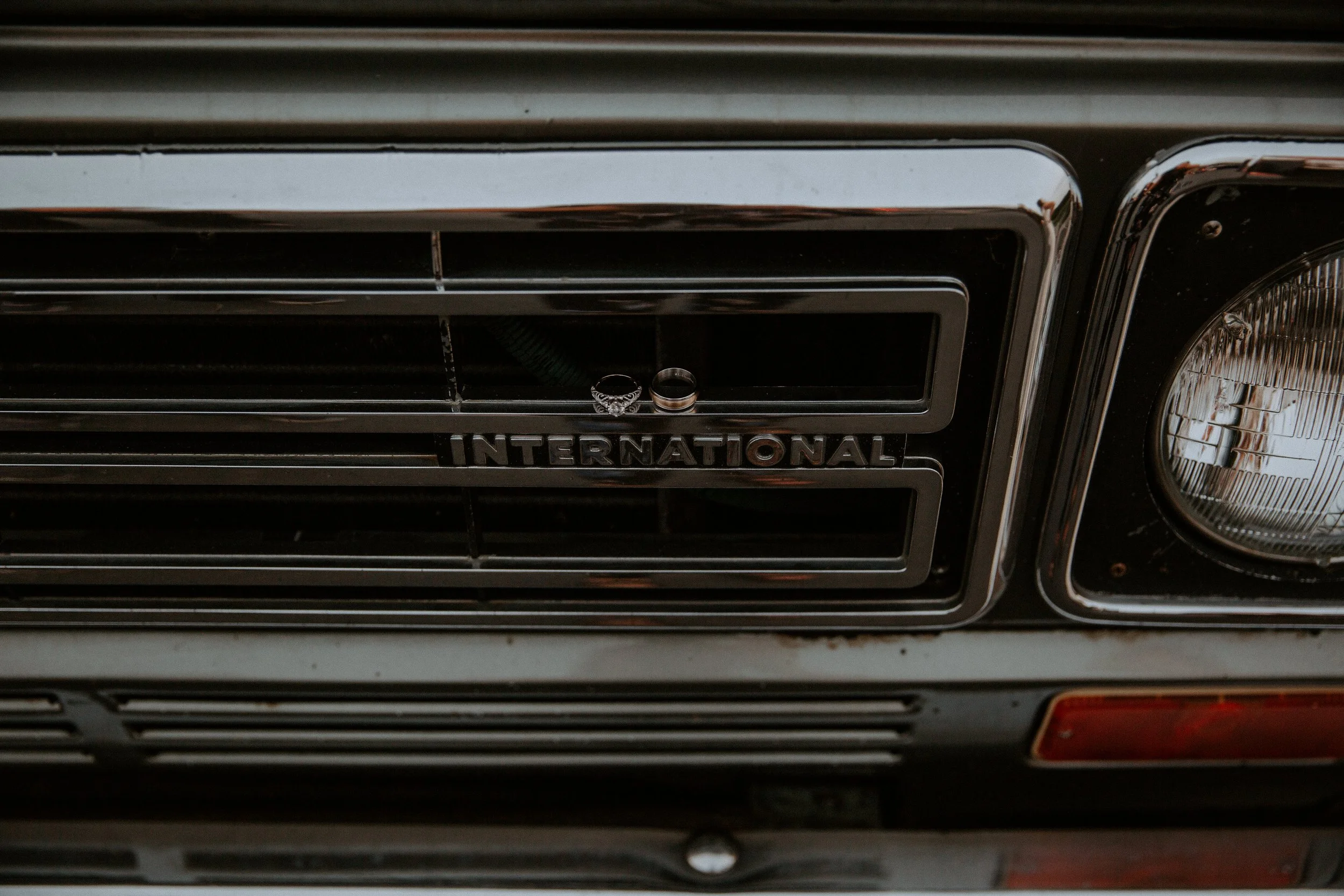 Close-up of wedding rings placed on the grille of a vintage "International" brand car, showcasing the car's logo.