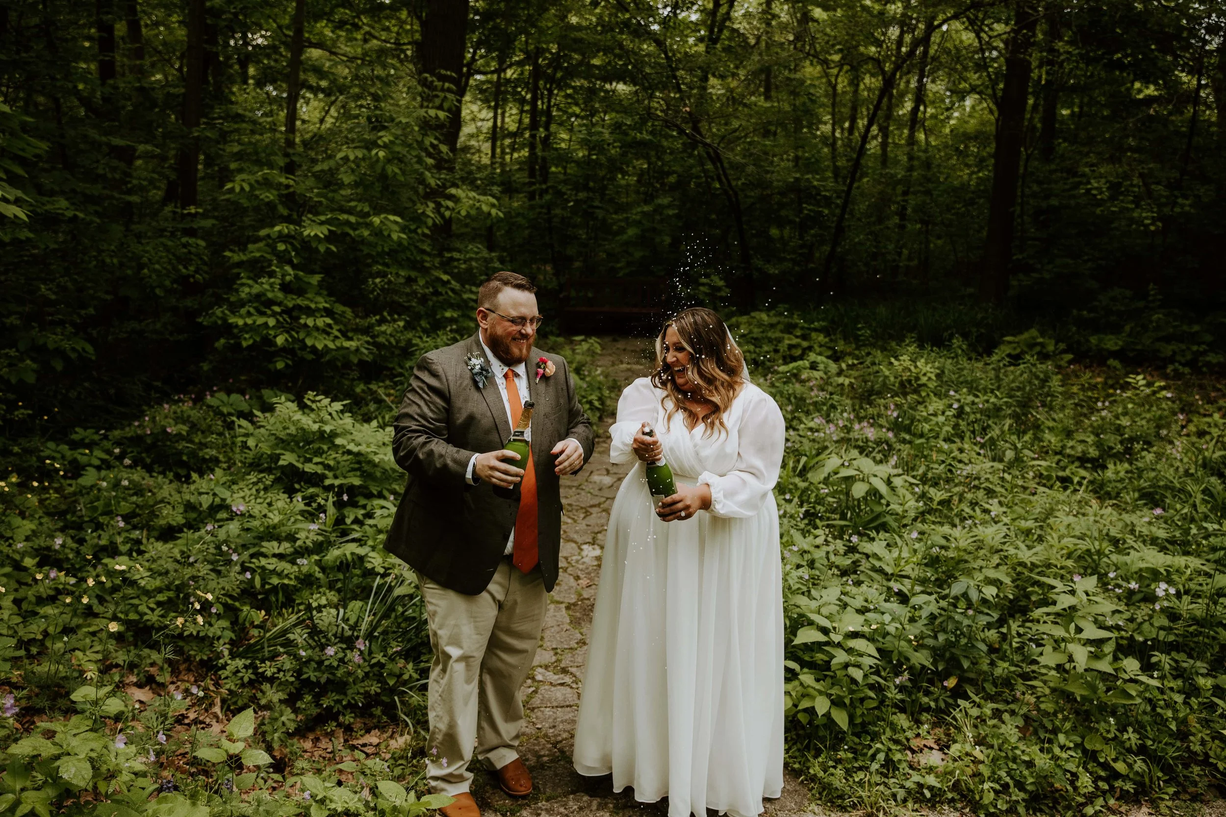 The bride and groom laugh at each other as they pop champagne.