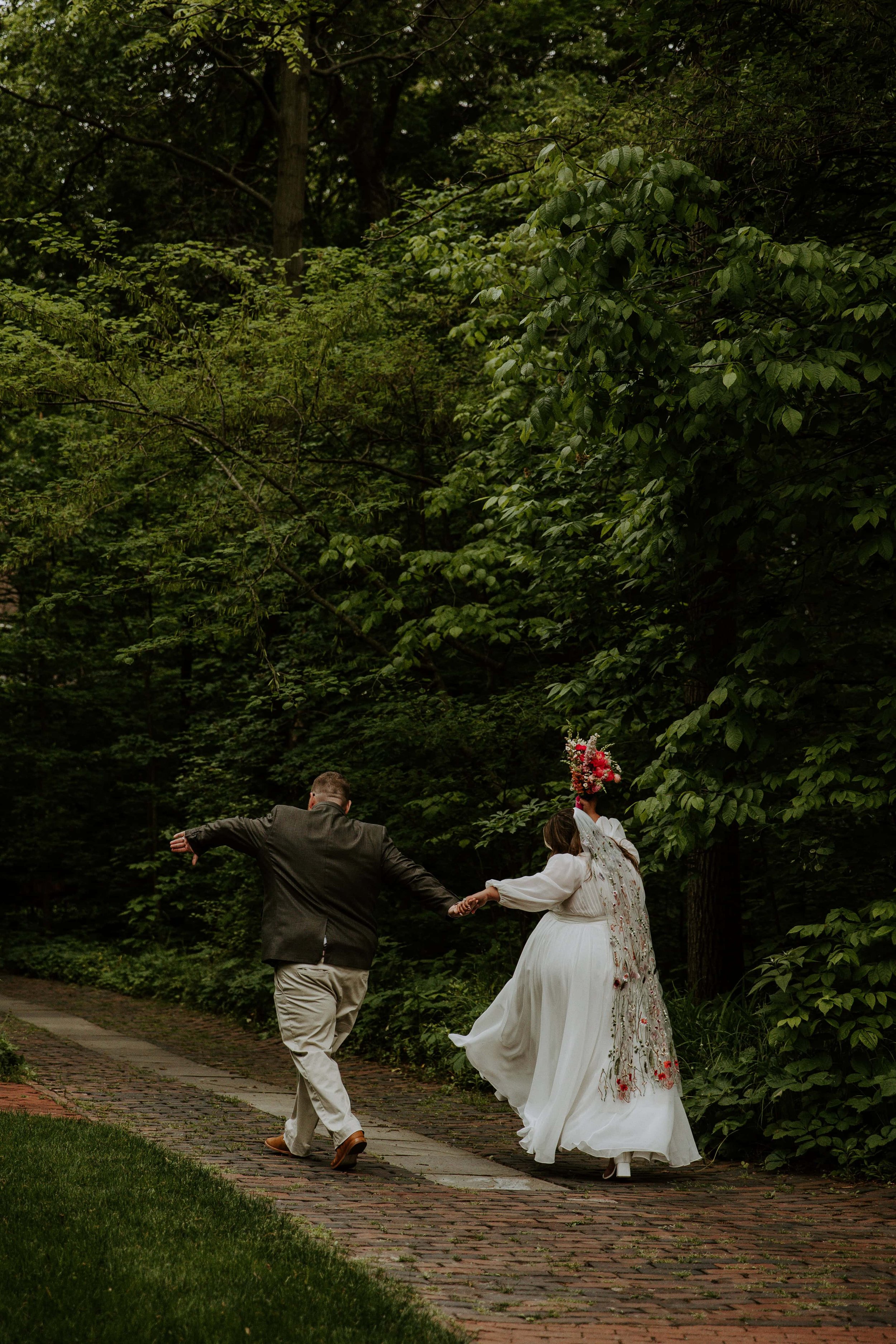 The bride and groom dance down the brick path surrounded by woods.