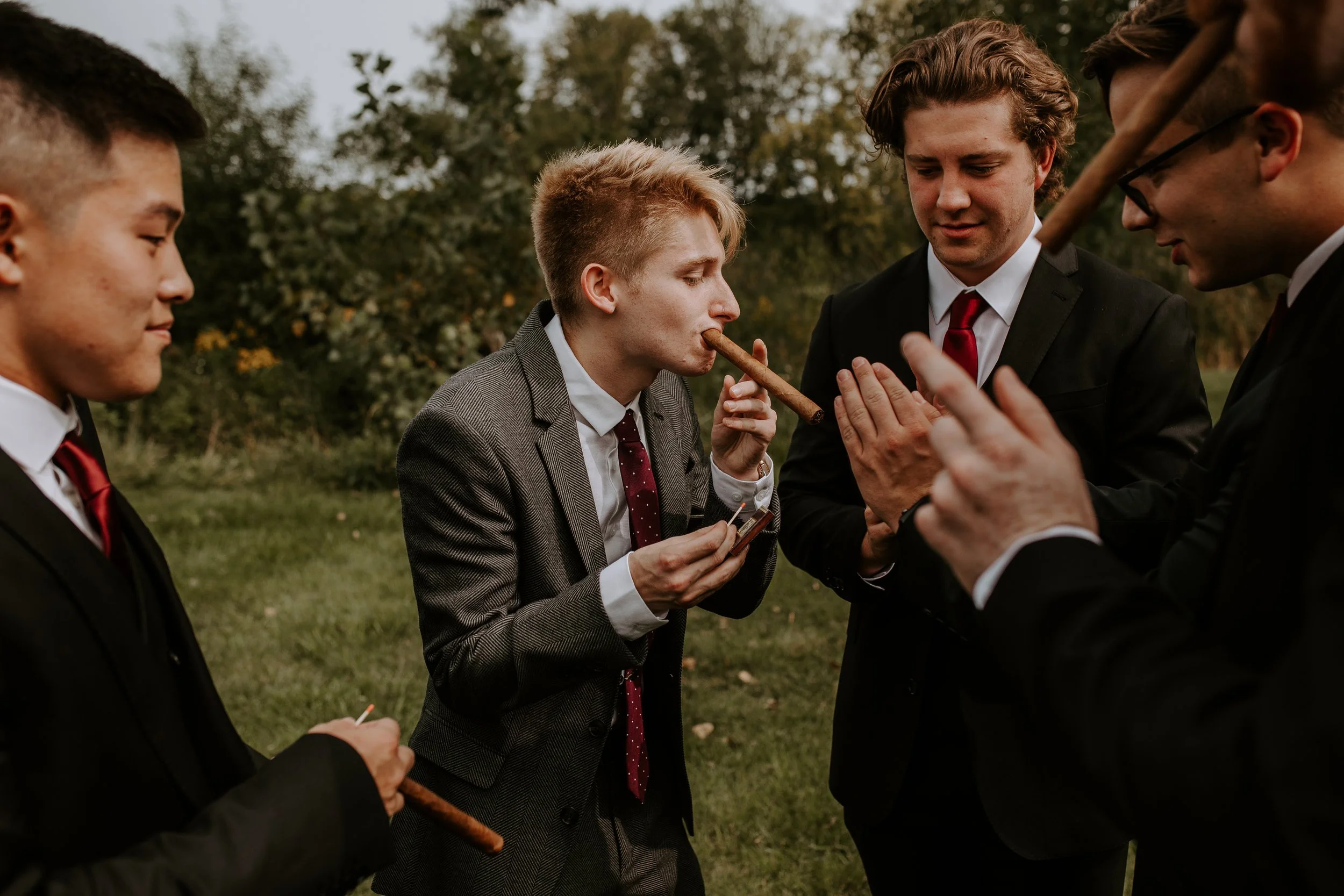 Groomsmen gather around as the groom lights a cigar, sharing a moment before the ceremony.