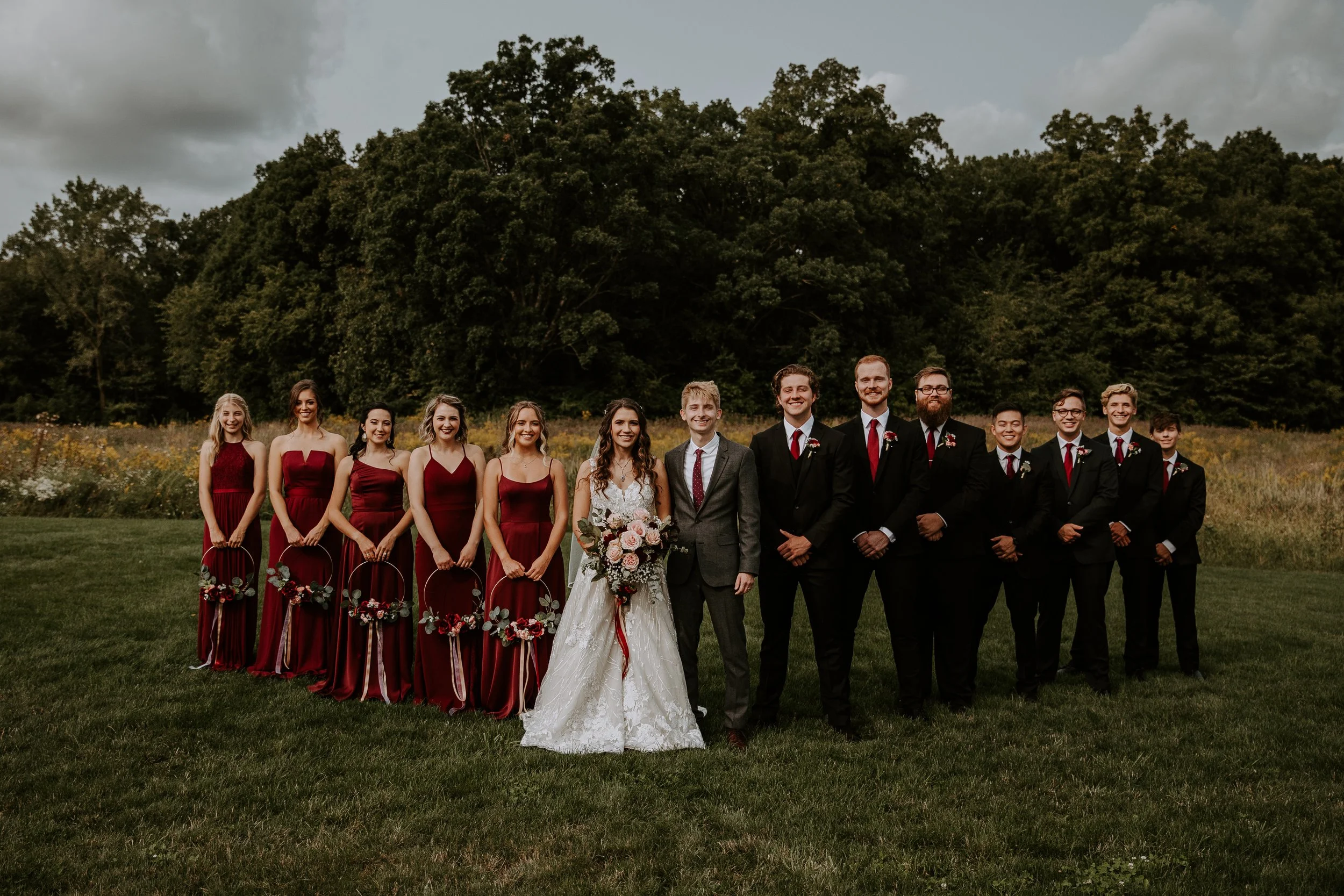 Bride and groom standing with their bridesmaids and groomsmen, all posed together in a line against a backdrop of greenery.