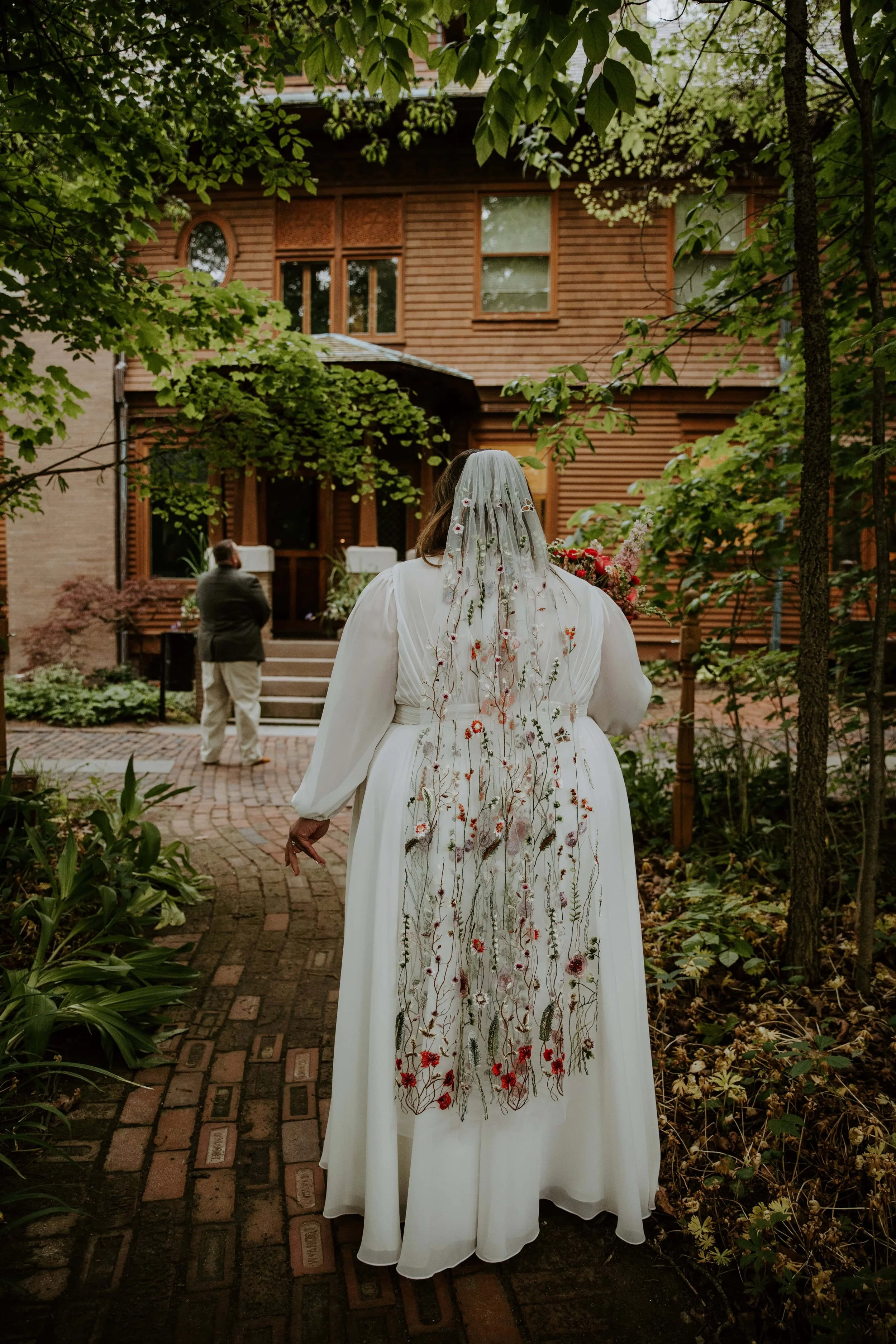 The brides back is to the camera as she walks to the groom for the first look with Oakhurst house in the background.