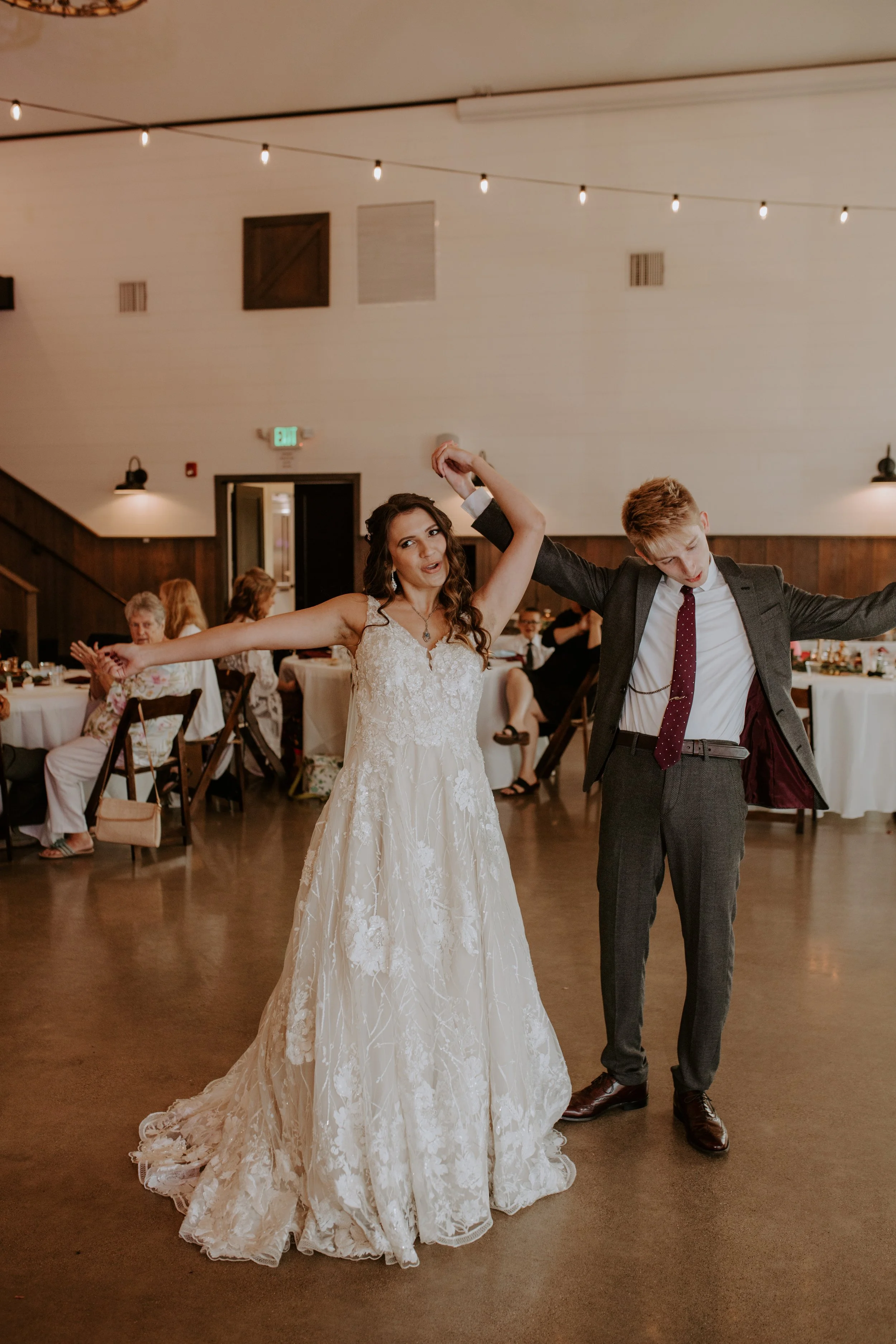 Bride and groom strike a playful pose on the dance floor, both smiling with arms outstretched.