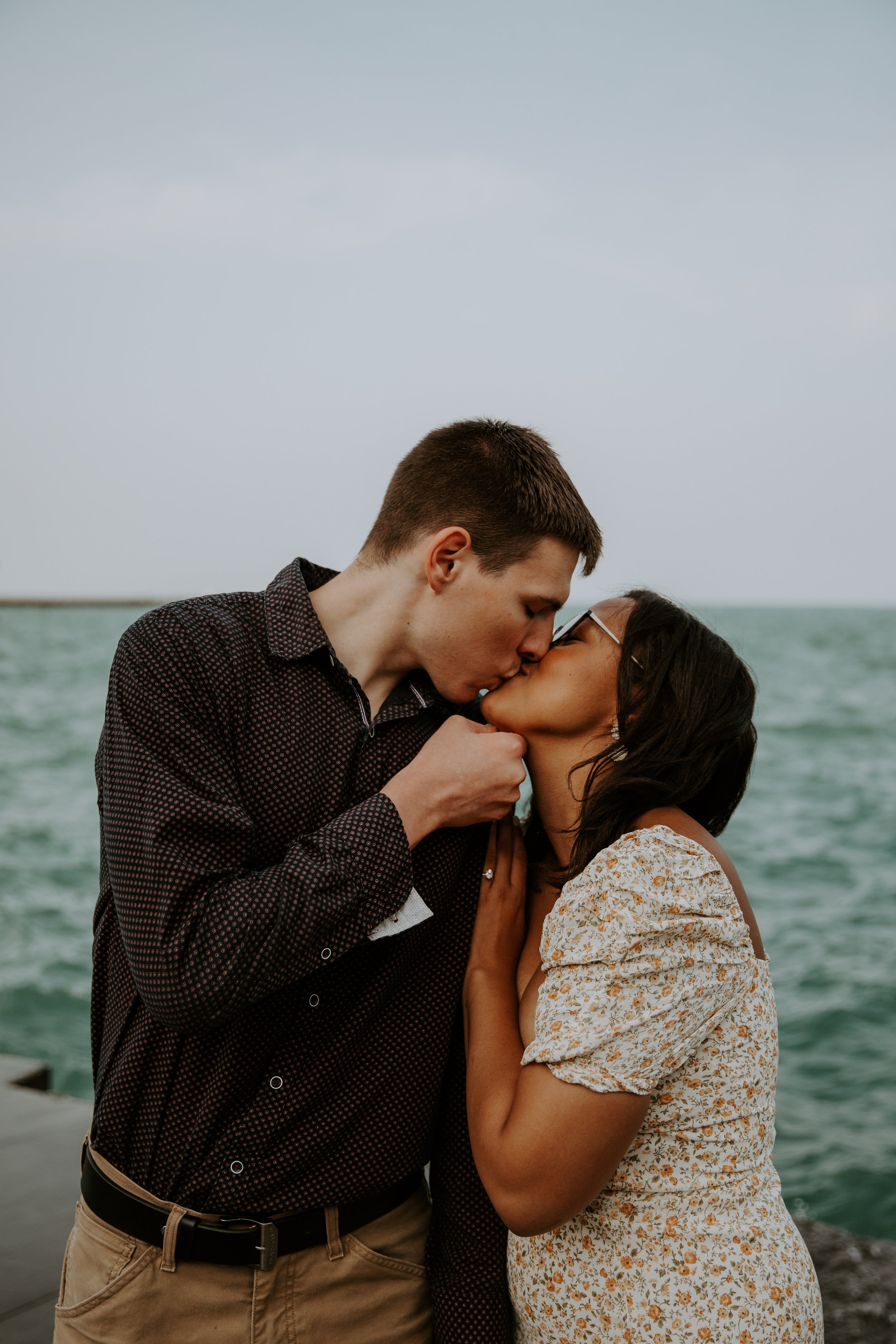 Couple sharing a kiss by the water during their engagement session with Lake Michigan in the background.