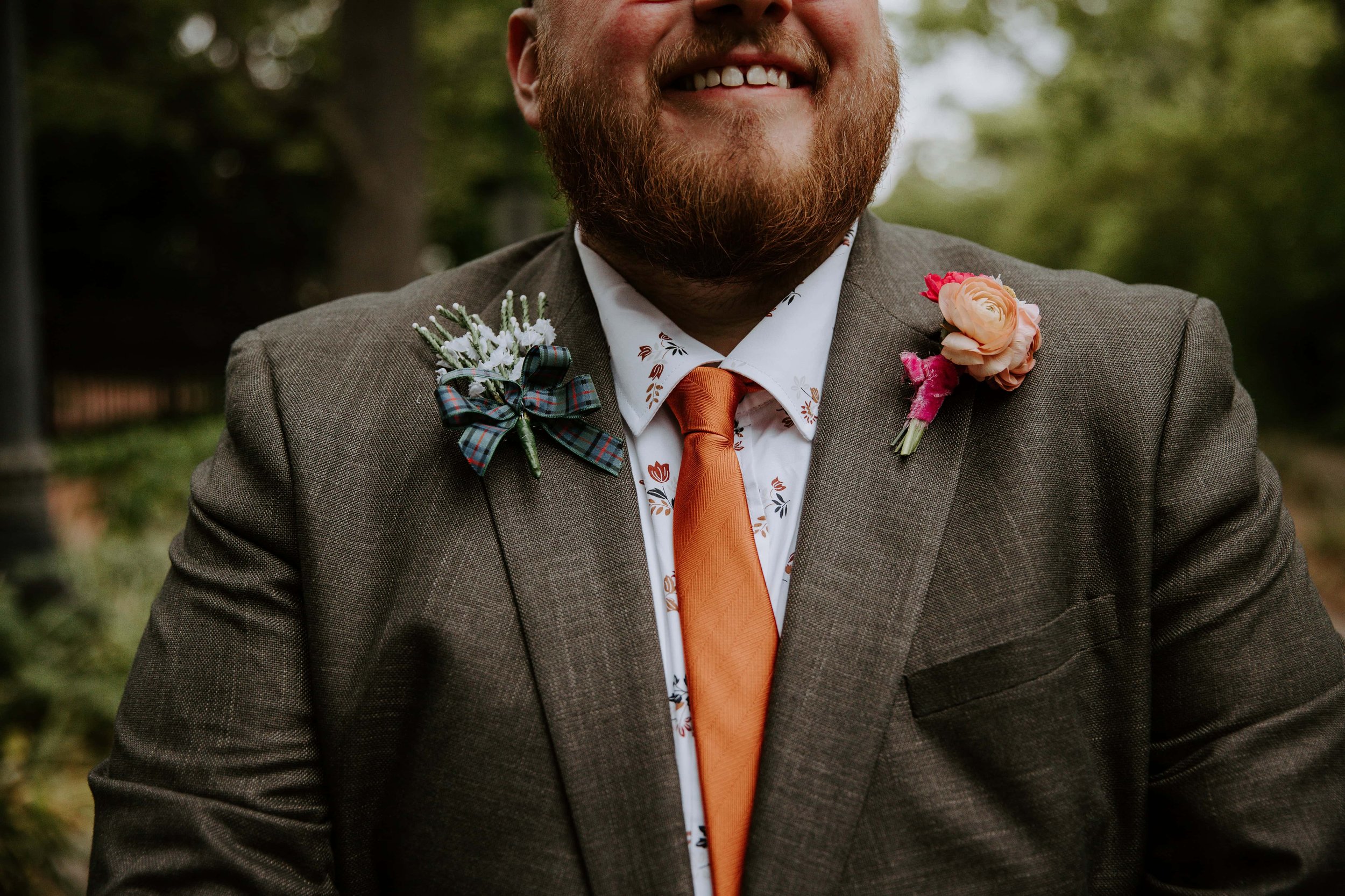 Portrait of the groom cut off so you can only see his smile and upper chest to show off the details of his floral shirt and boutonniere.