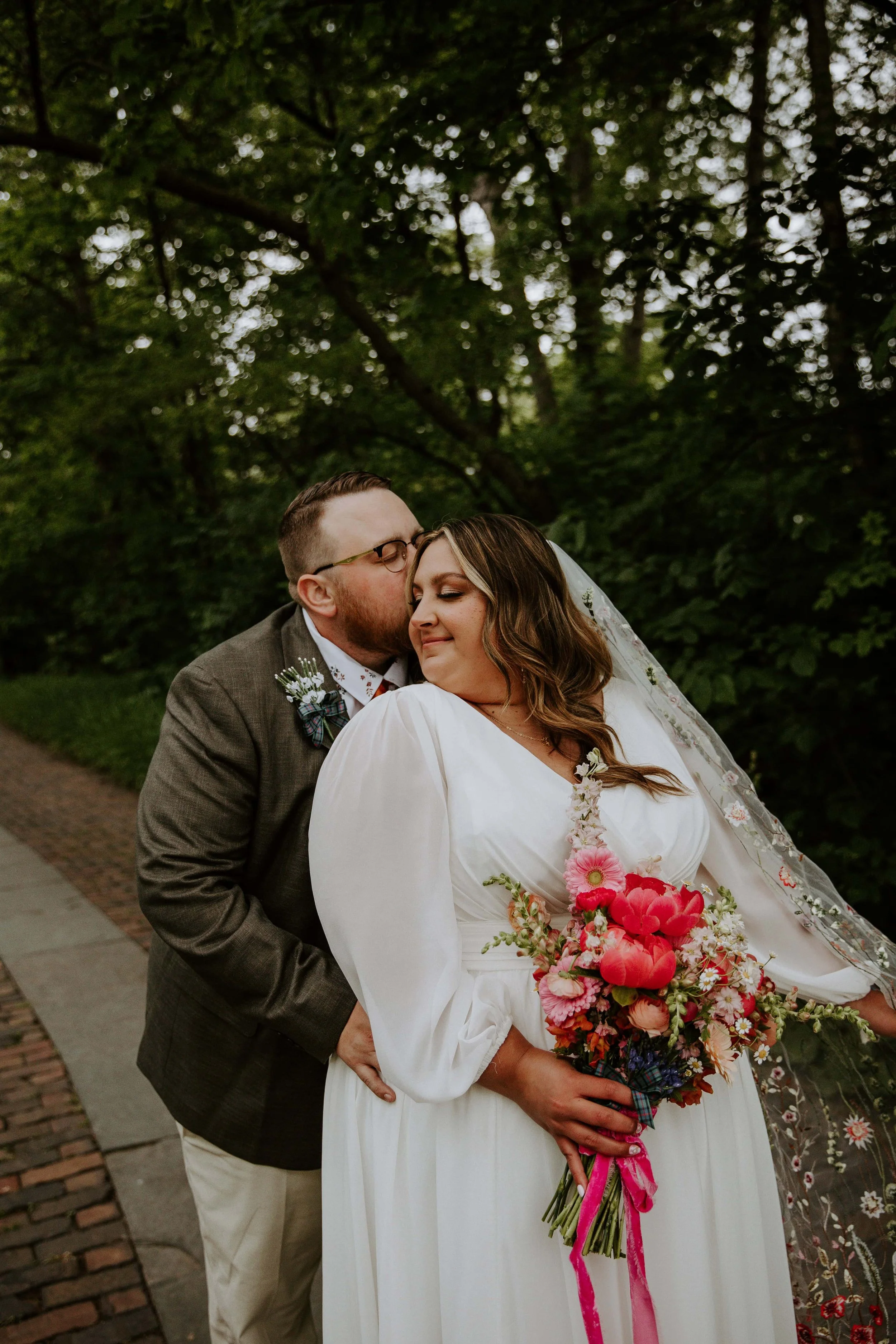 The groom kisses the bride on the temple while she sways her floral veil.