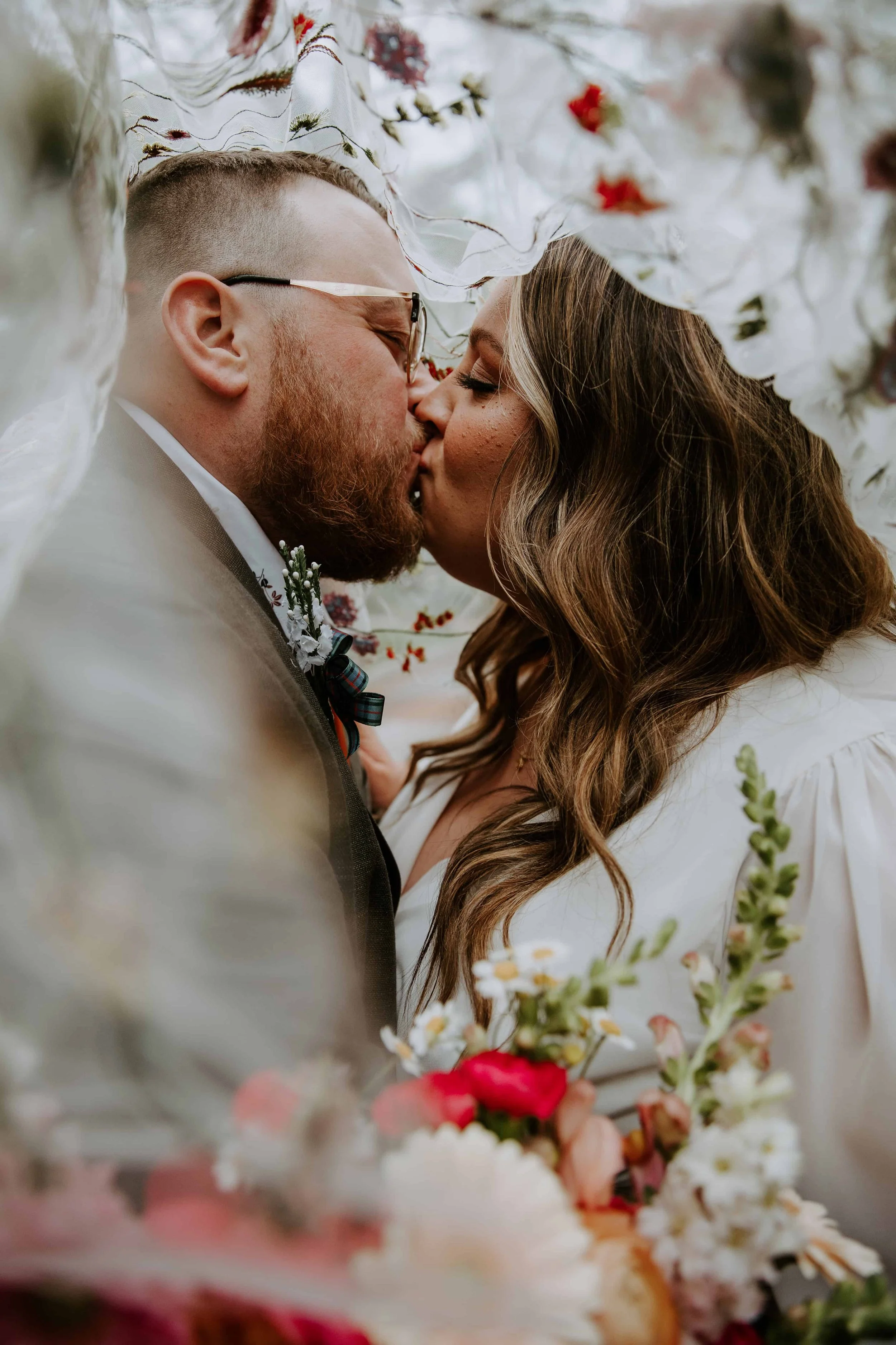 The bride and groom kiss underneath the bride's floral veil.