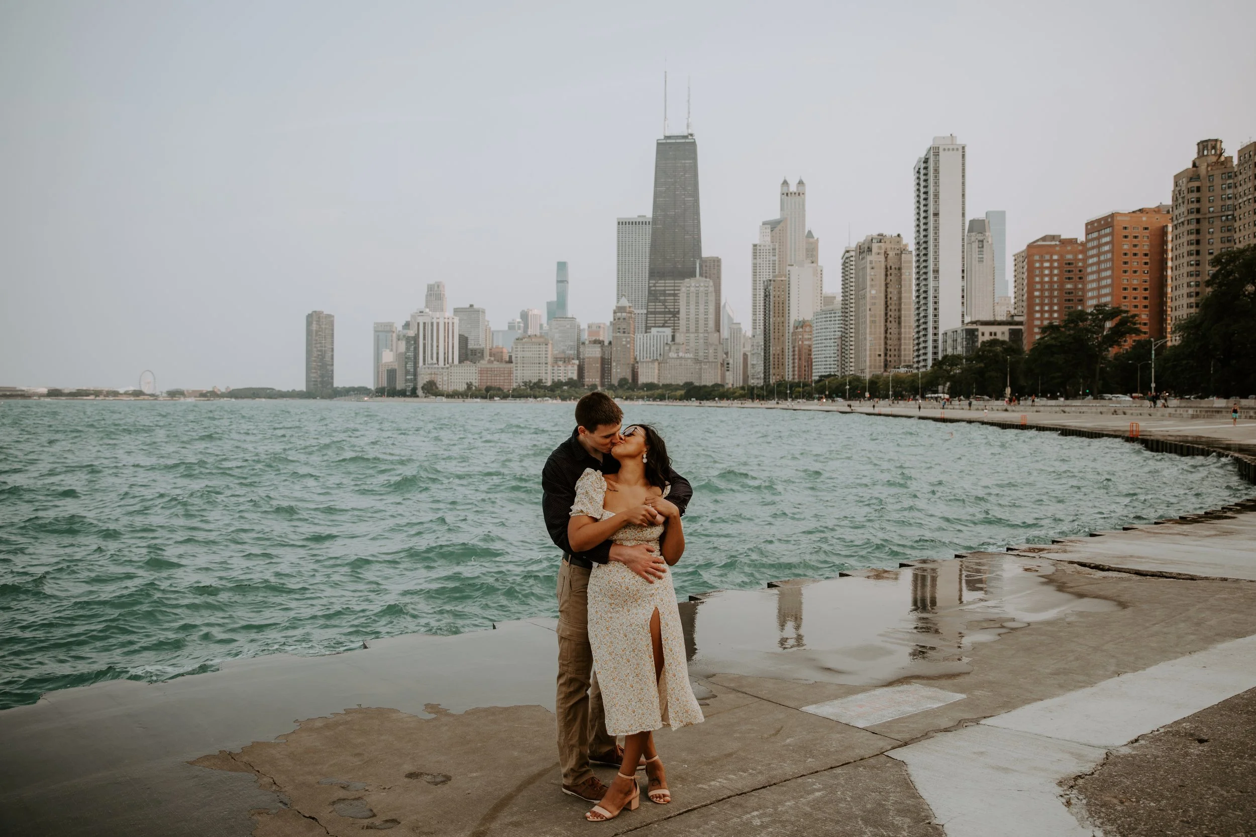 Couple embracing by Lake Michigan with the Chicago skyline in the background at North Beach.