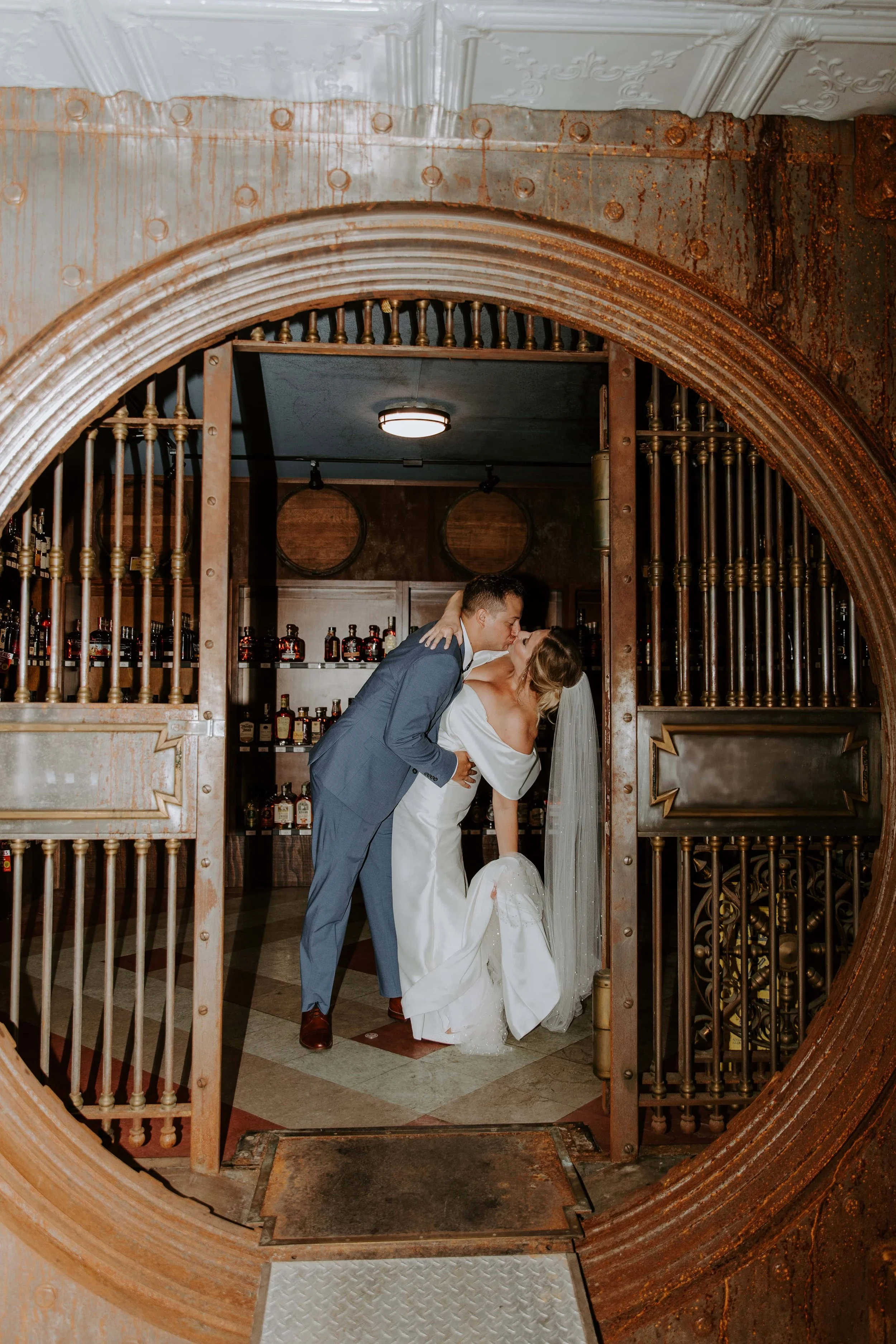 The bride and groom kiss in the open doorway of a whiskey vault